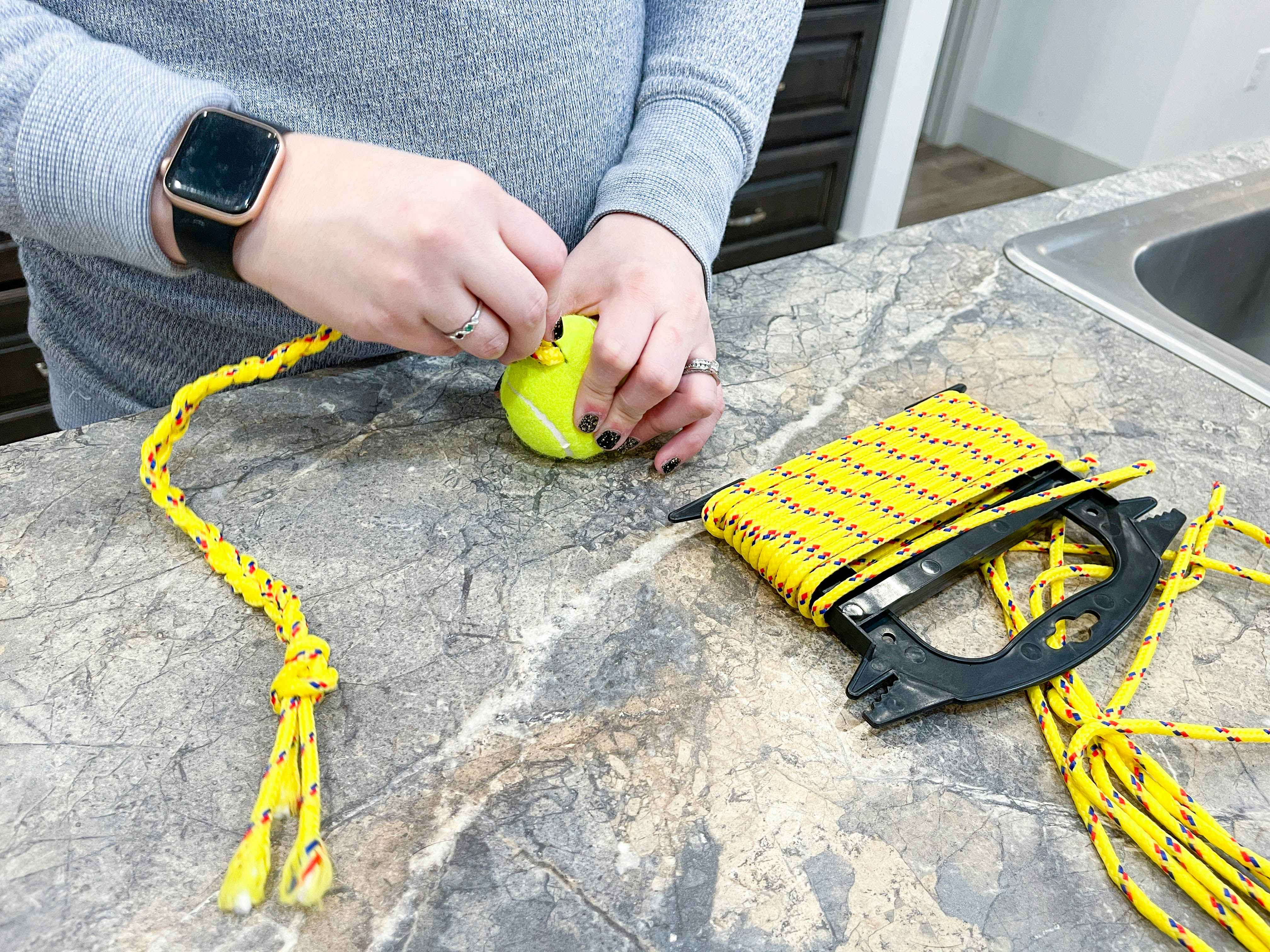 a person cutting a tennis ball next to rope to make a diy dog toy 