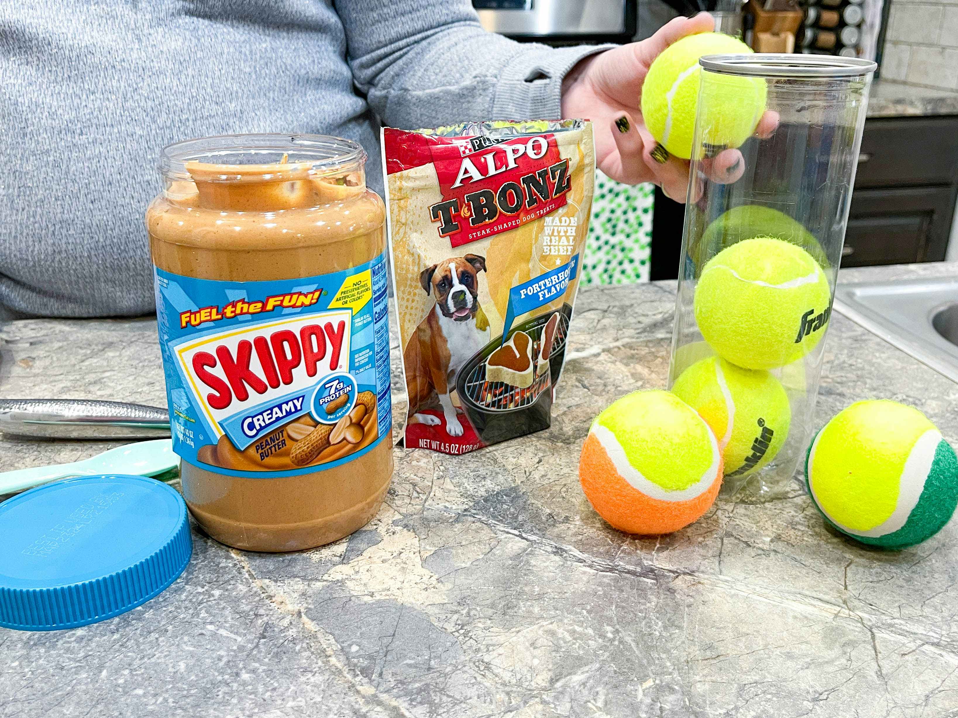 a person holding a tennis ball next to dog treats and peanut butter