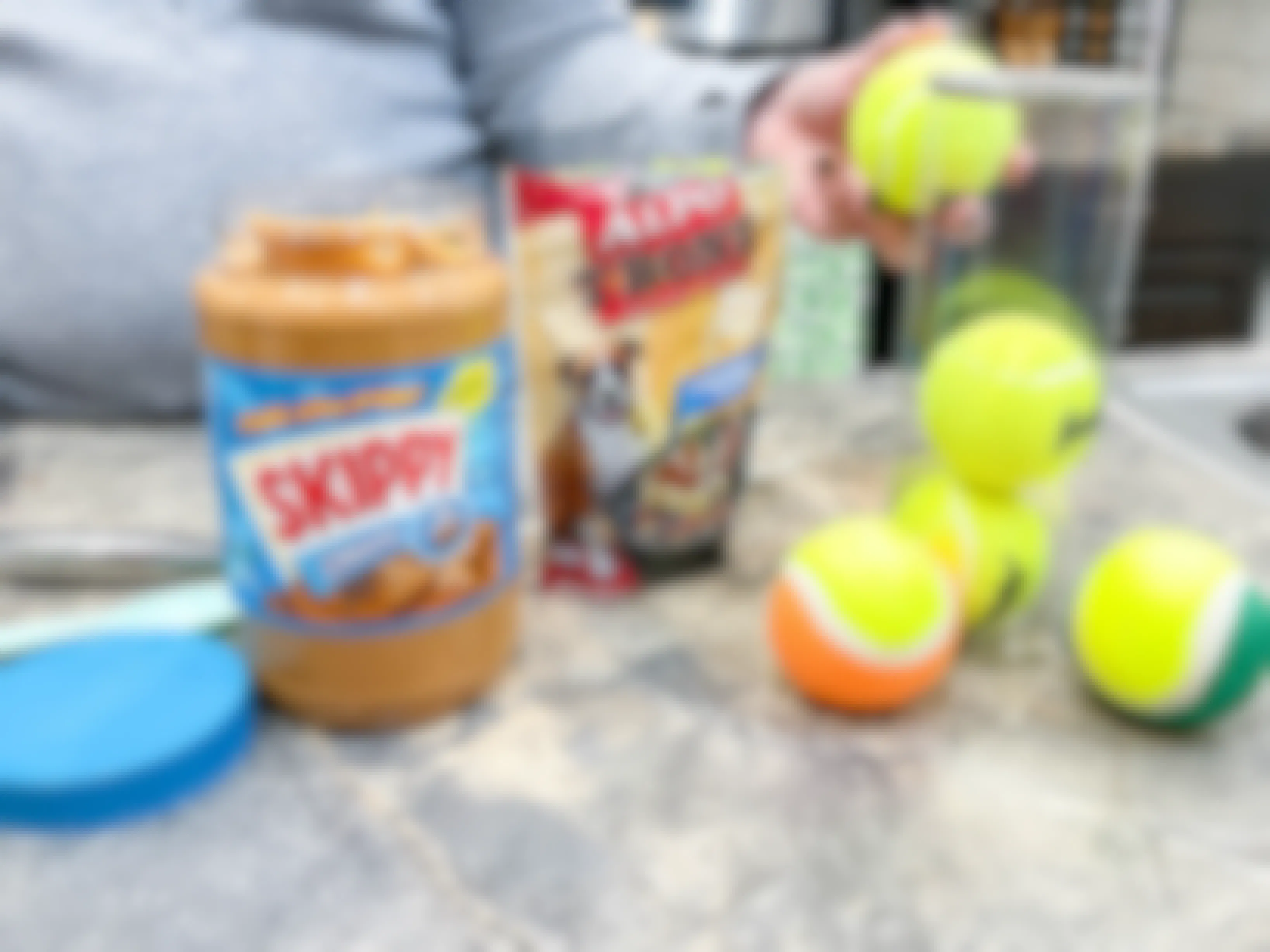 a person holding a tennis ball next to dog treats and peanut butter