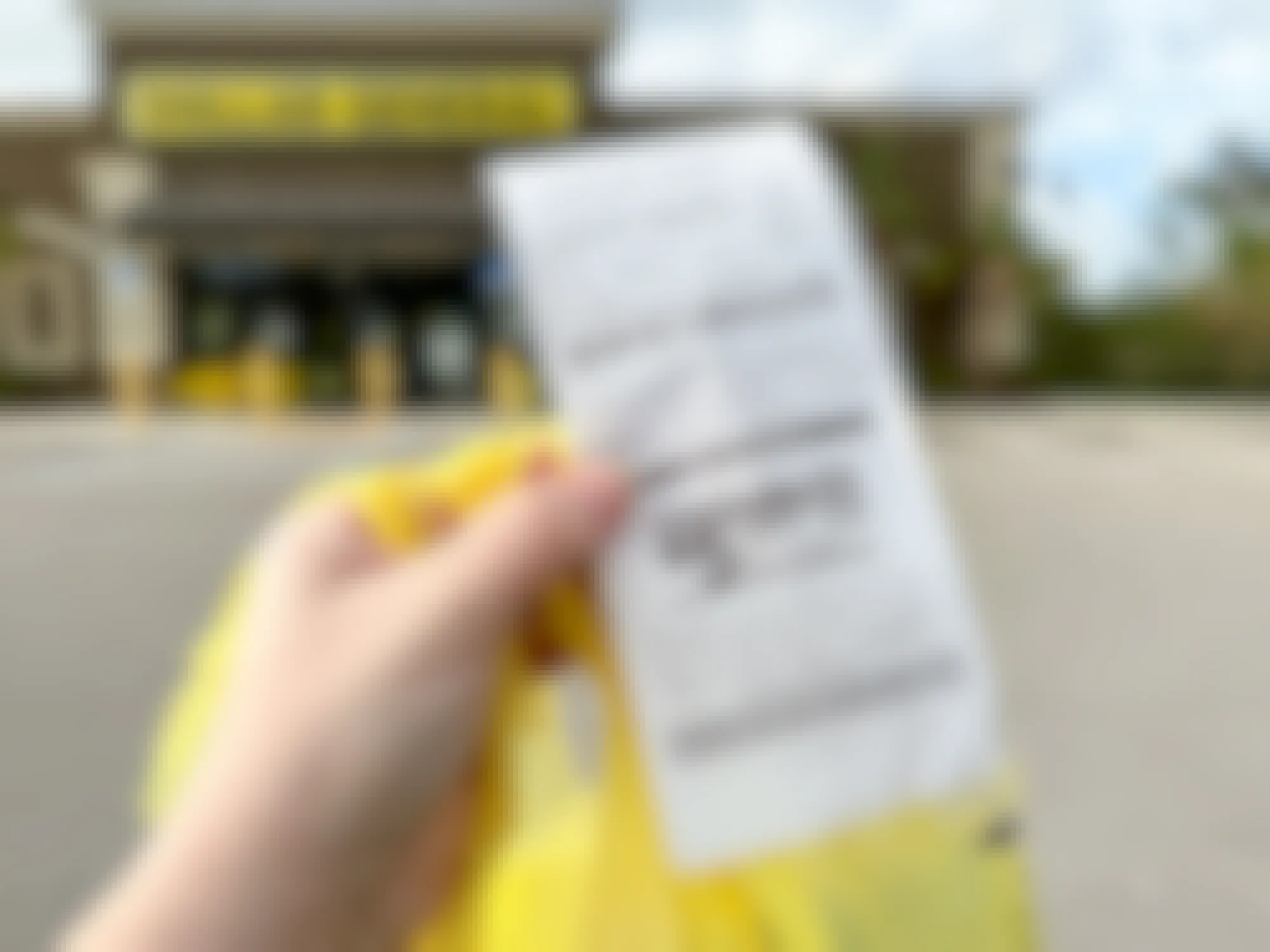 Someone holding a Dollar General receipt with a bag outside of a Dollar General