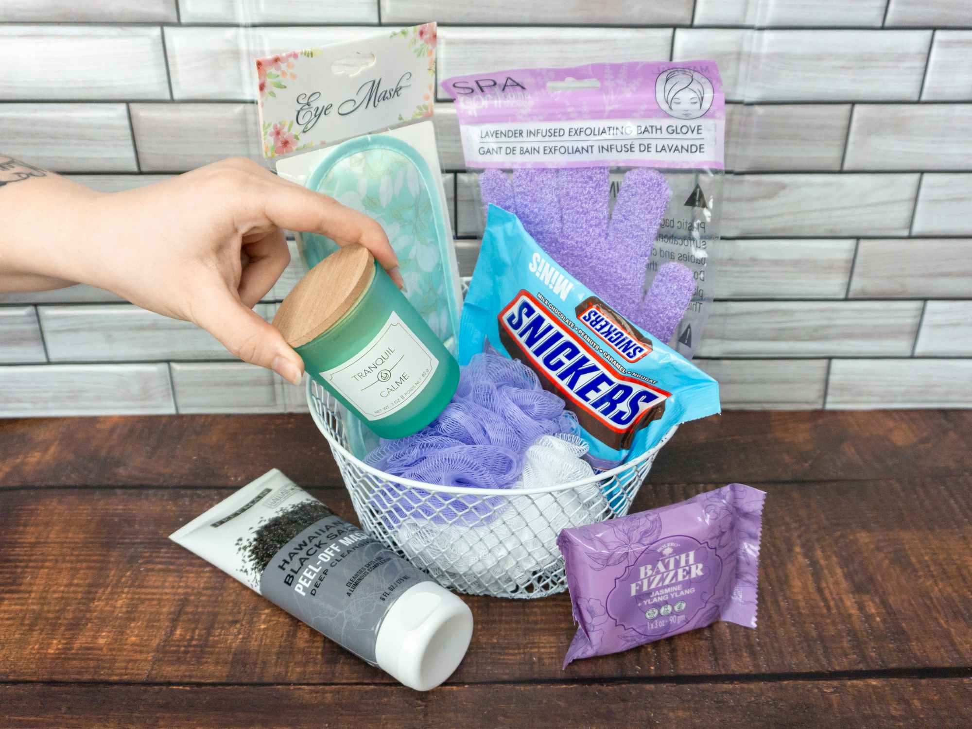 Someone putting a Dollar Tree candle into a spa themed gift basket