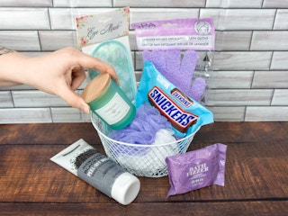 Someone putting a Dollar Tree candle into a spa themed gift basket