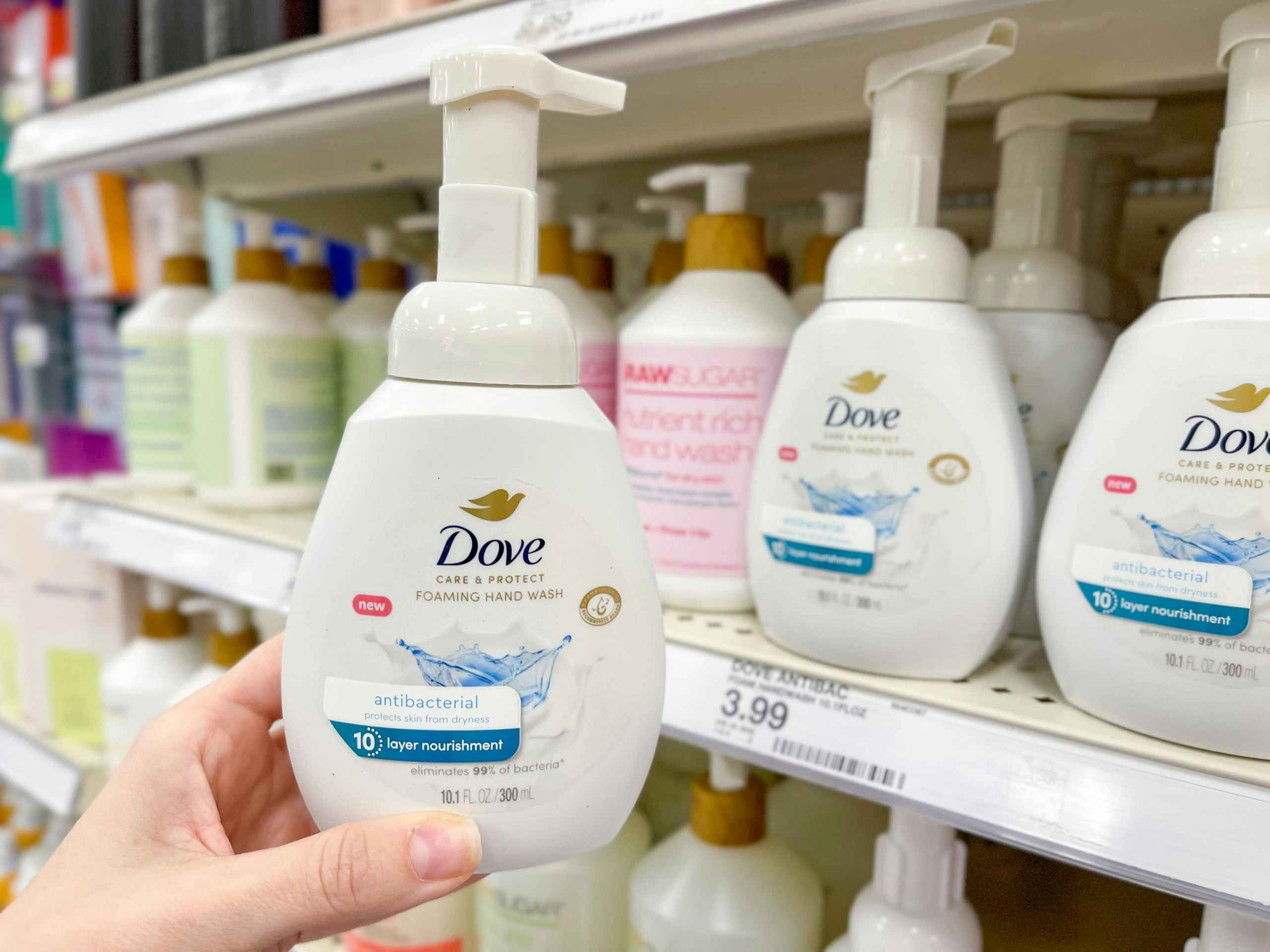 A Dove hand soap held out by hand next to other Dove hand soaps sitting on a store shelf.