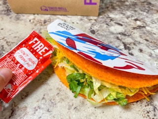 a person putting fire sauce onto a doritos locos taco