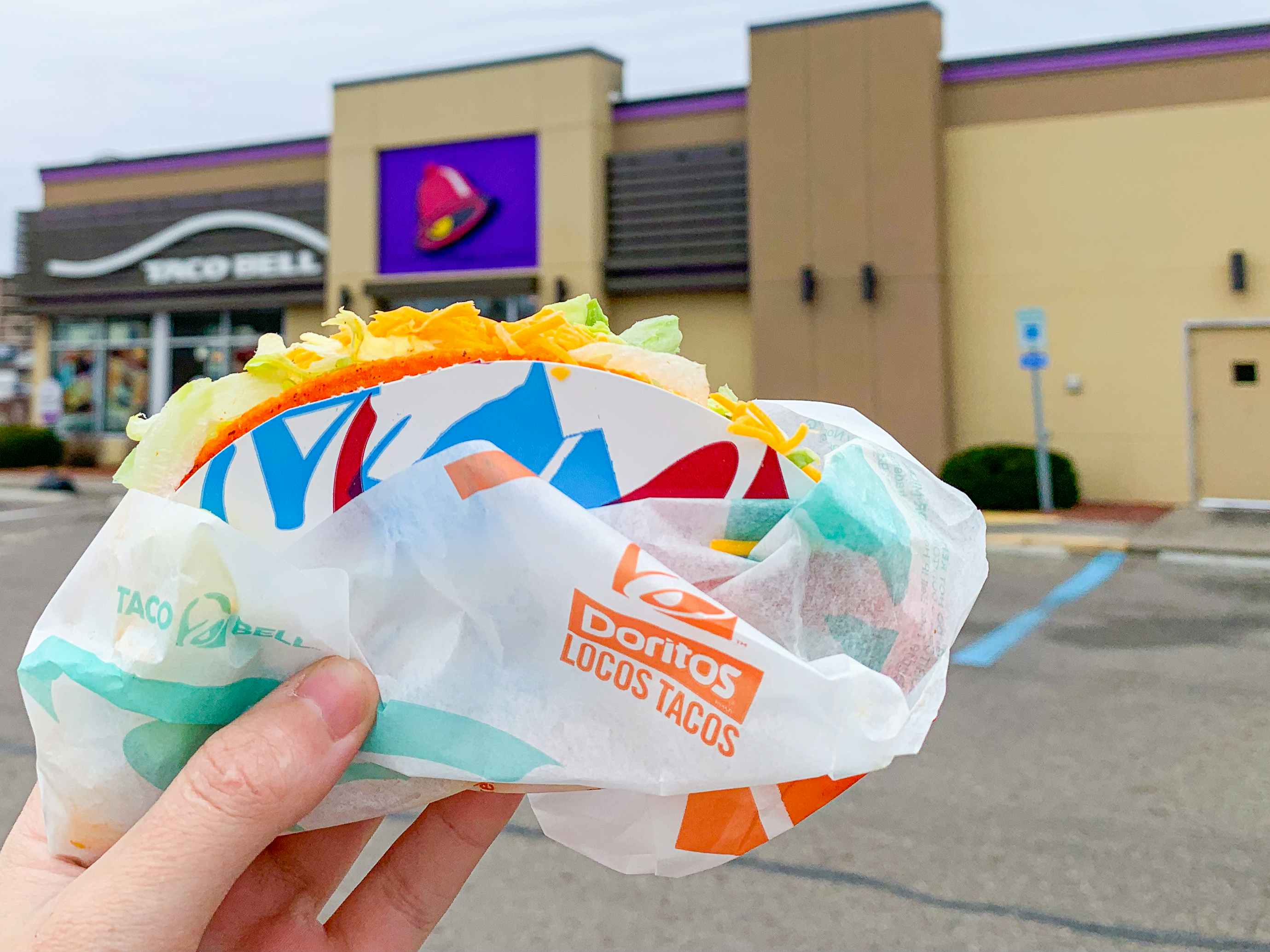 a person holding a doritos locos taco outside of a taco bell