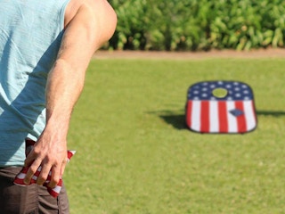 person throwing bags and playing cornhole game in yard