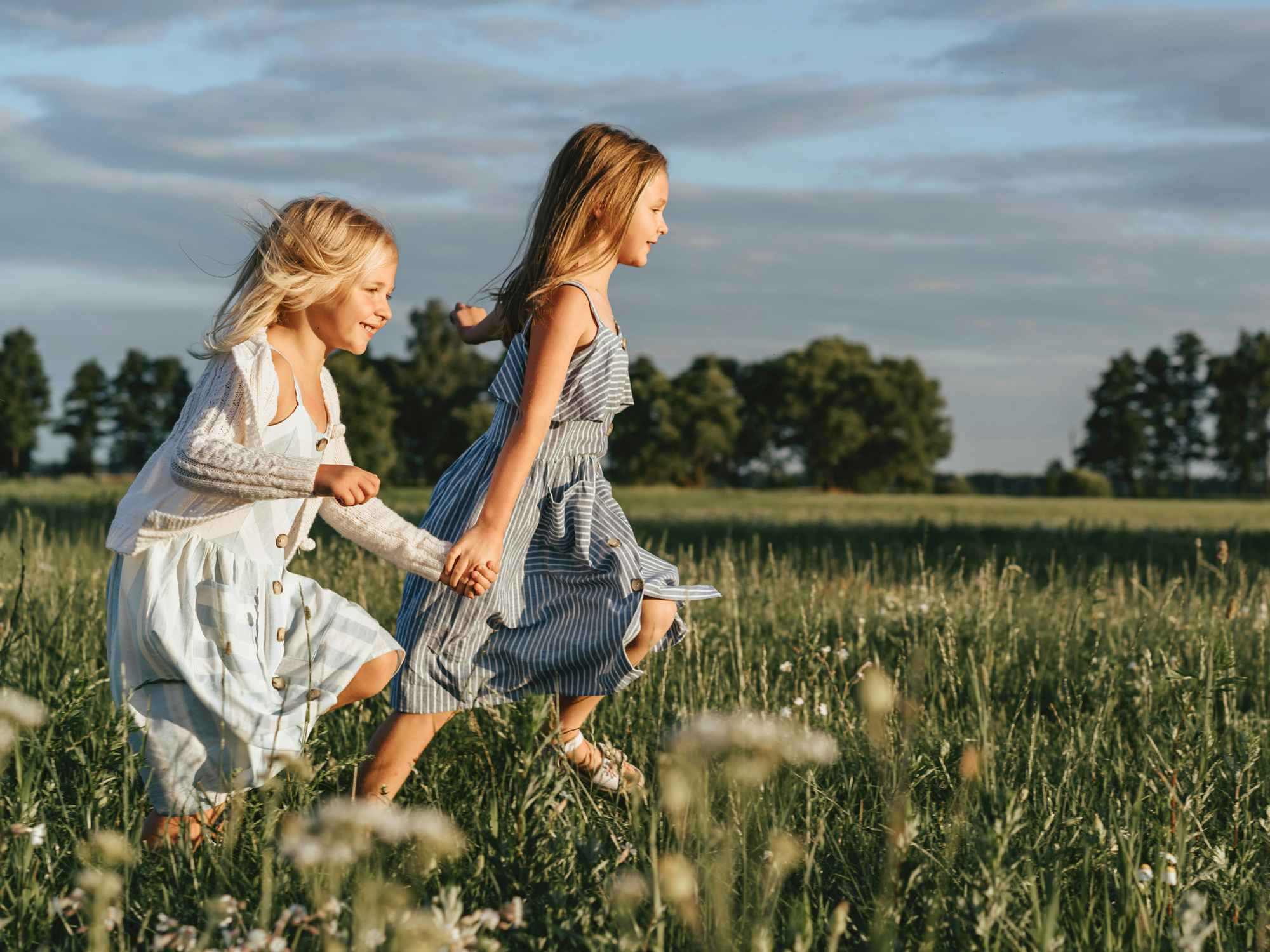 two girls in dresses running in a field