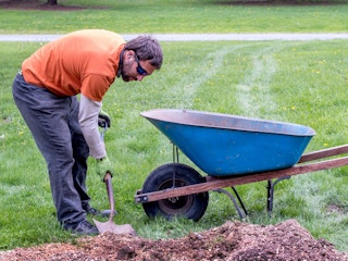person shoveling mulch into their wheelbarrow