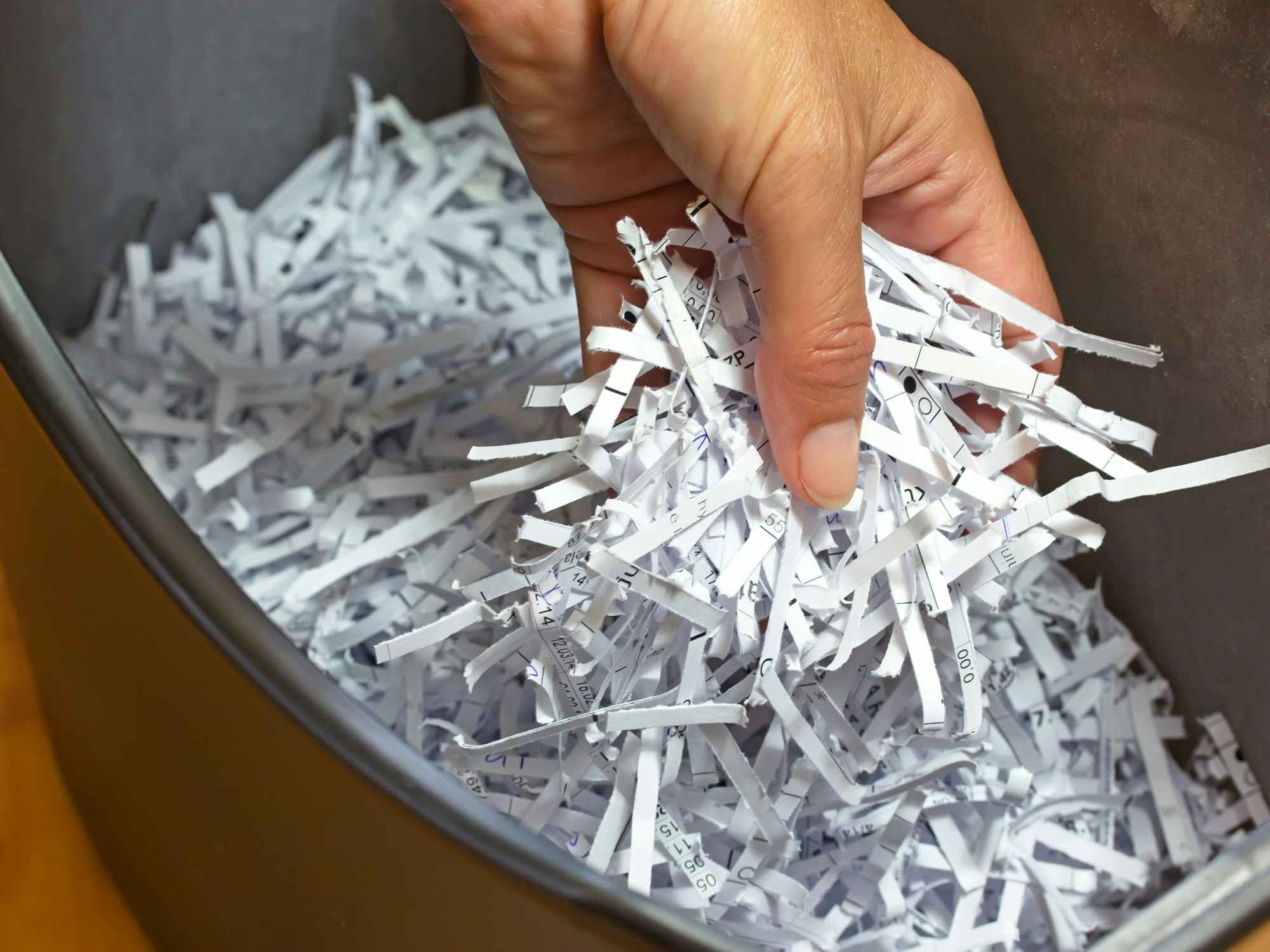 Someone holding a handful of shredded paper above a bin full of paper shreds