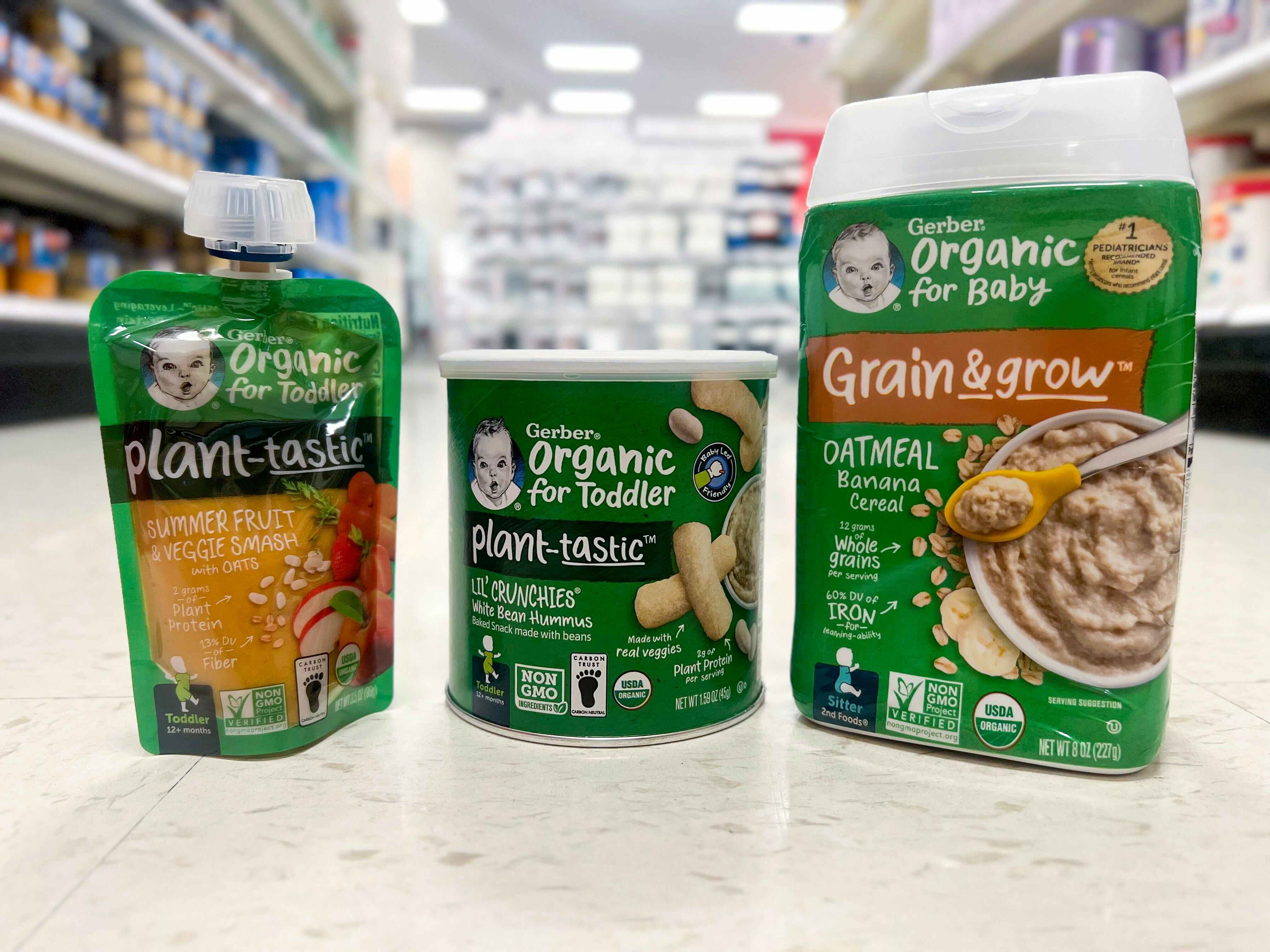 Three Gerber Organic baby products lined up on the supermarket floor: Oatmeal banana cereal, plant-tastic lil' crunchies, and plant-tastic summer fruit and veggie smash with oats