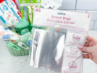 a person's hand holding a dollar store basket bag in front of a gift basket