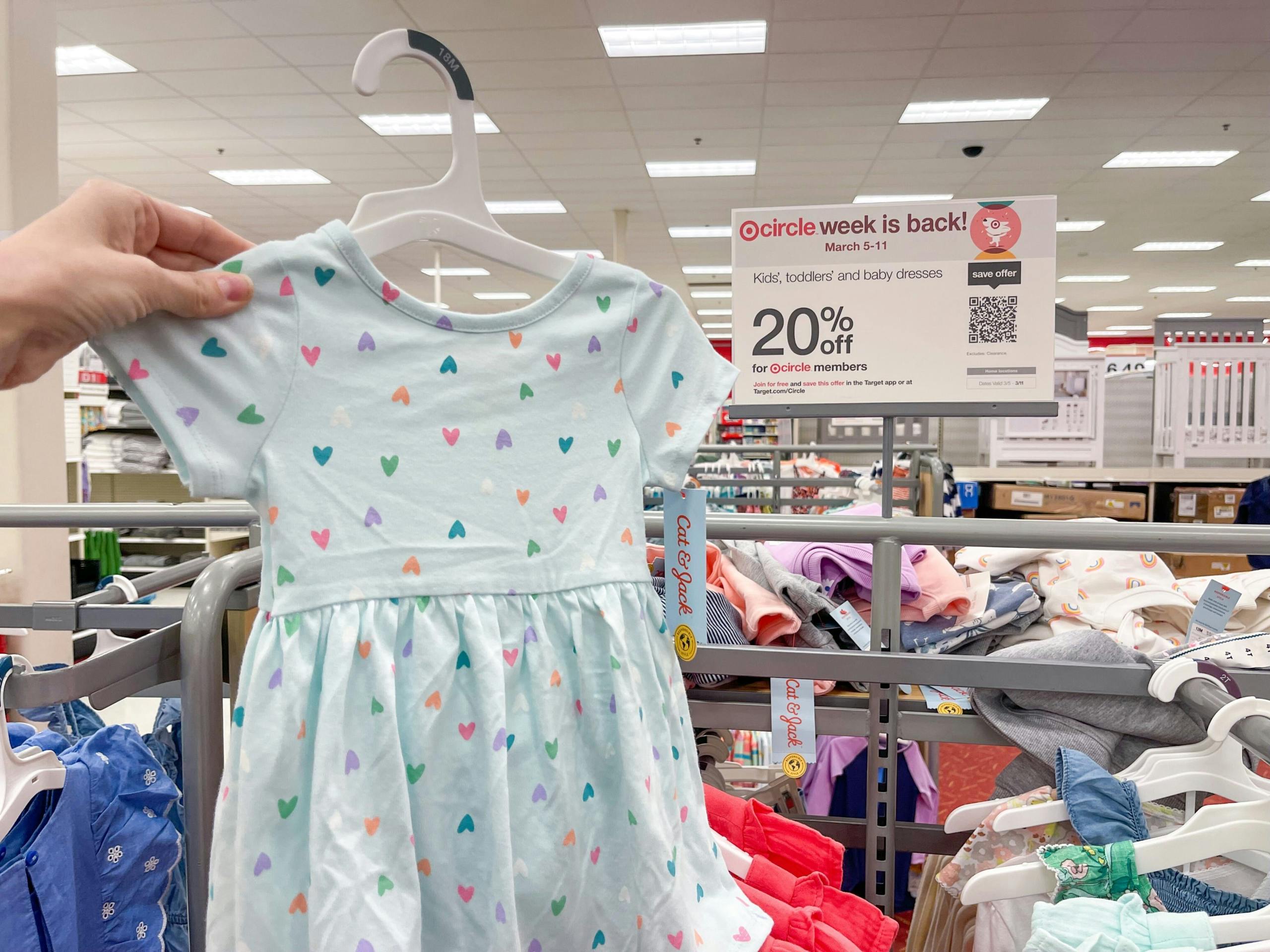 A toddler girls dress held out by hand in front of a sale sign.