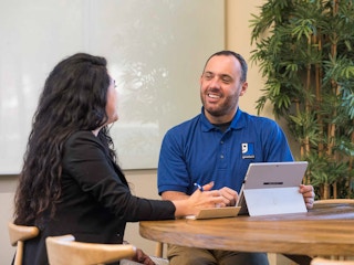 A person wearing a Goodwill shirt talking to someone at a table
