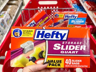 A box of hefty bags held out by hand in front of a store shopping cart with other hefty boxes sitting in it