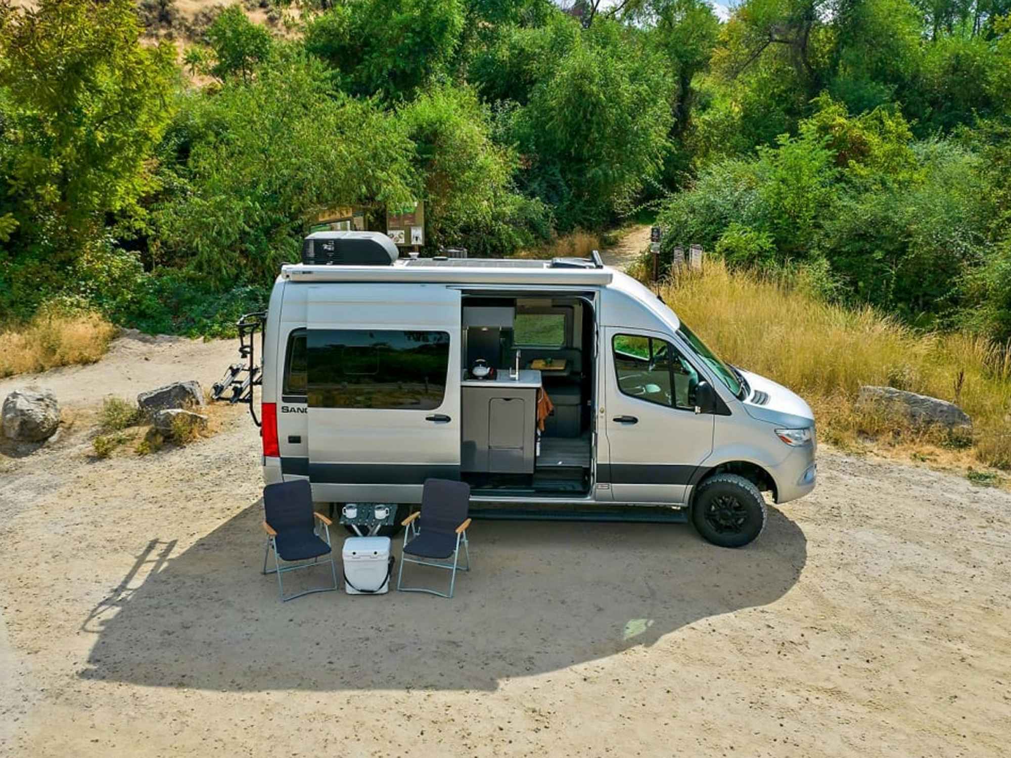 a van with the doors open with lawn chairs outside of it