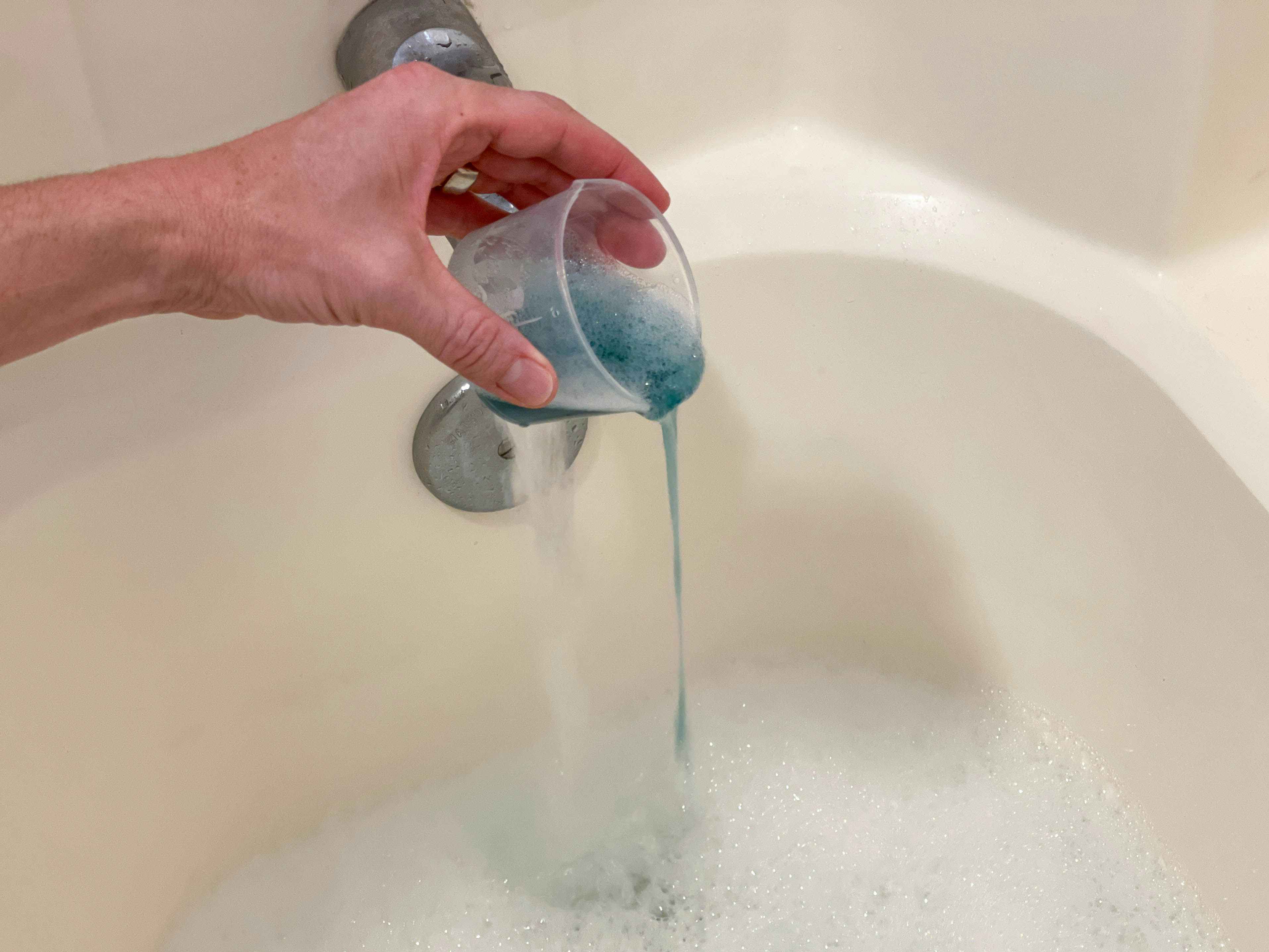 a person adding liquid detergent to a bathtub 