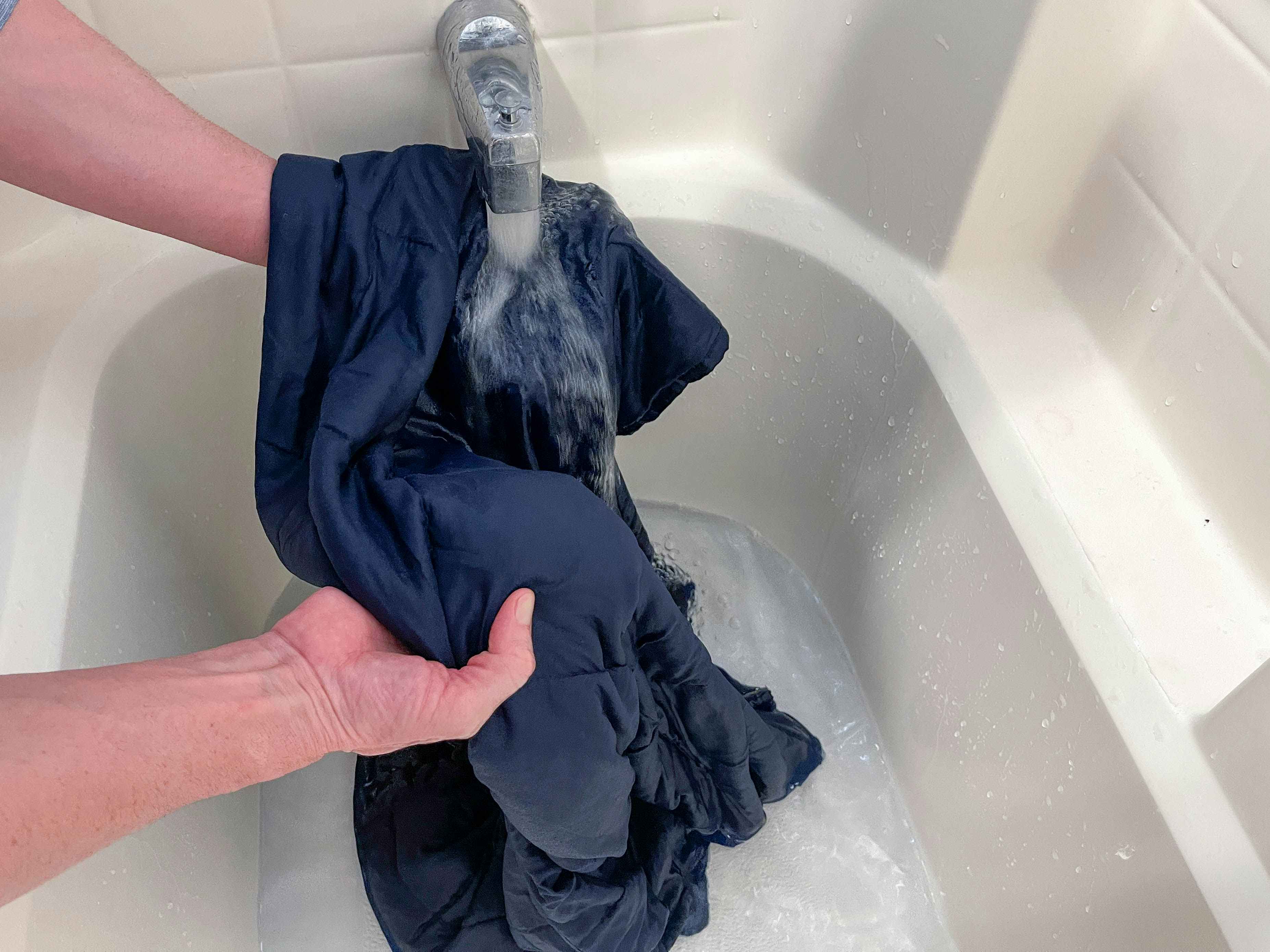 a person rinsing a weighted blanket in a bathtub 
