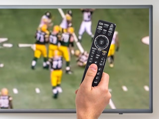 person watching nfl sunday ticket and holding remote