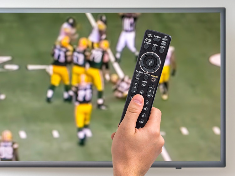 person watching nfl sunday ticket and holding remote