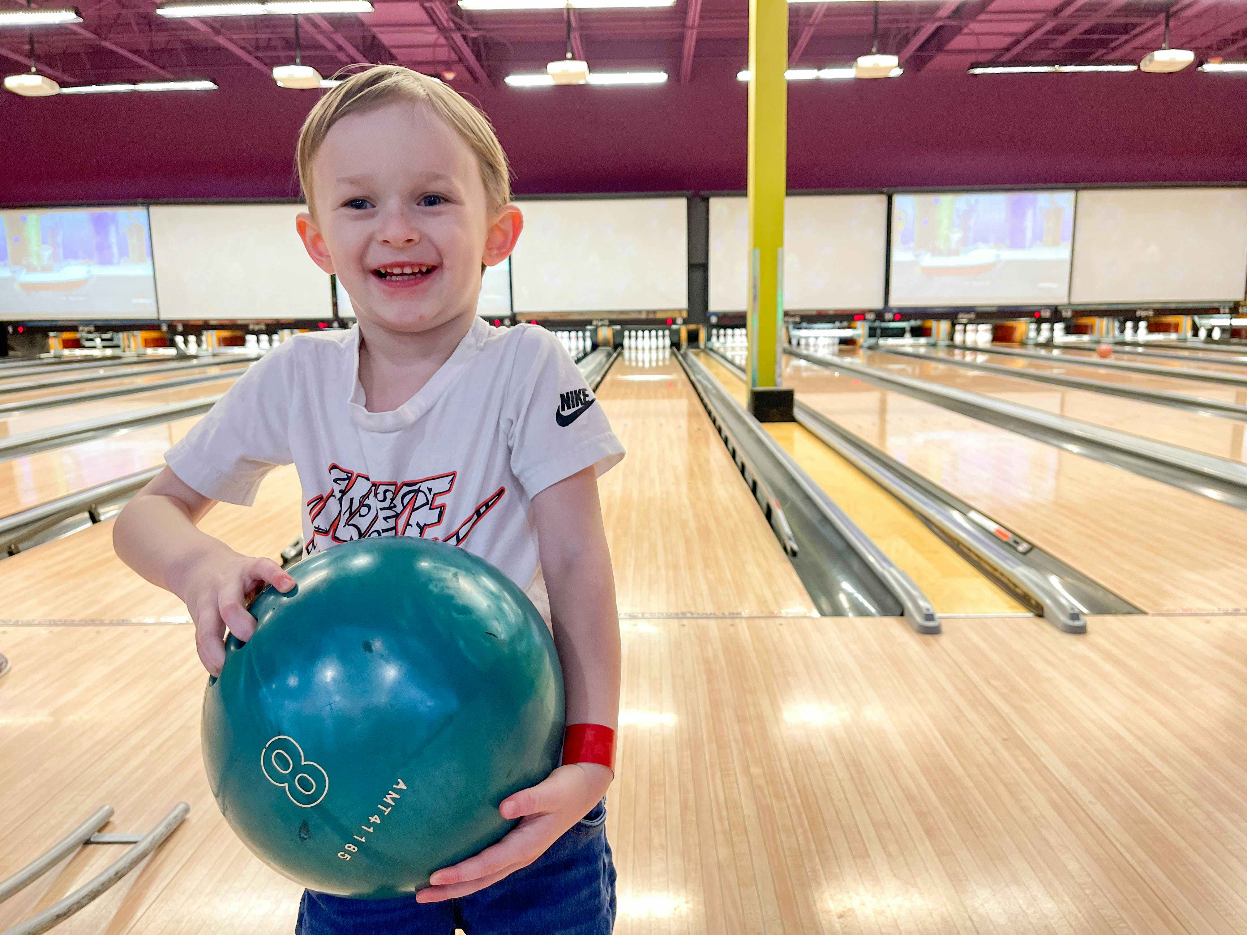 a child smiling and holding a bowling ball at a bowling alley