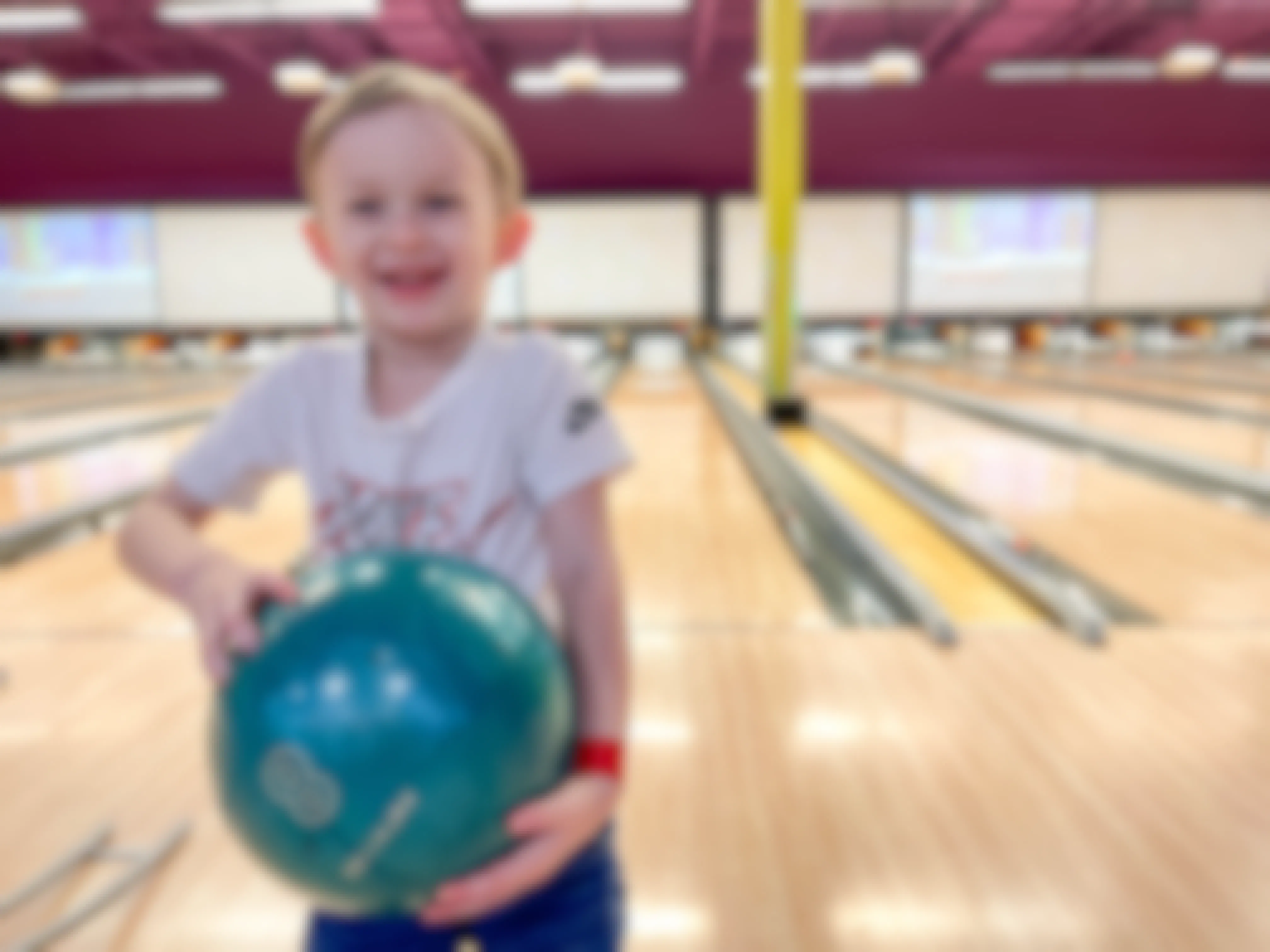 a child smiling and holding a bowling ball at a bowling alley