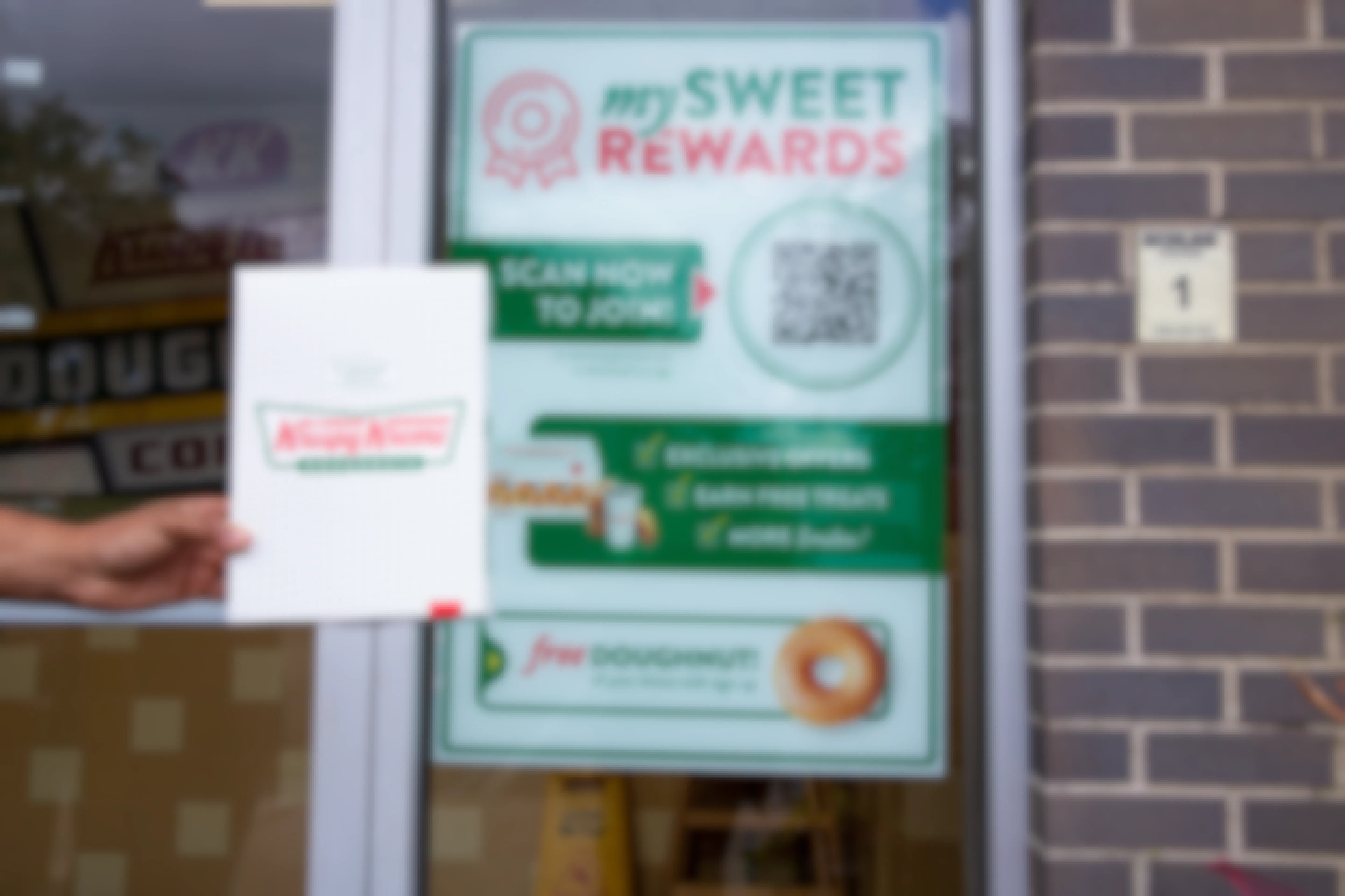 a person holding a bag of krispy Kreme donuts in front of rewards signage 
