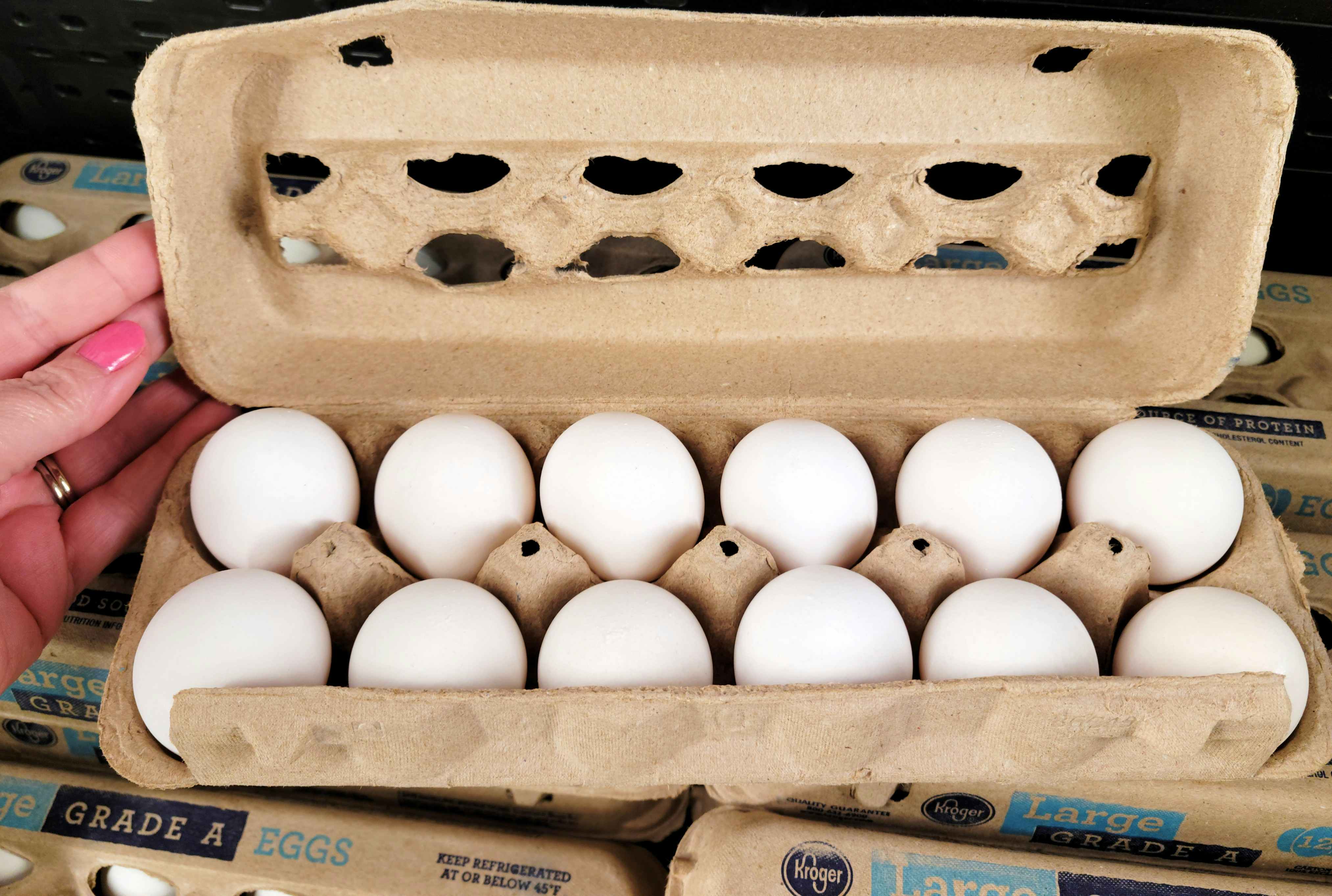persons hand holding open a carton of a dozen eggs in a store