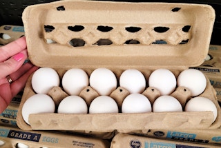 persons hand holding open a carton of a dozen eggs in a store