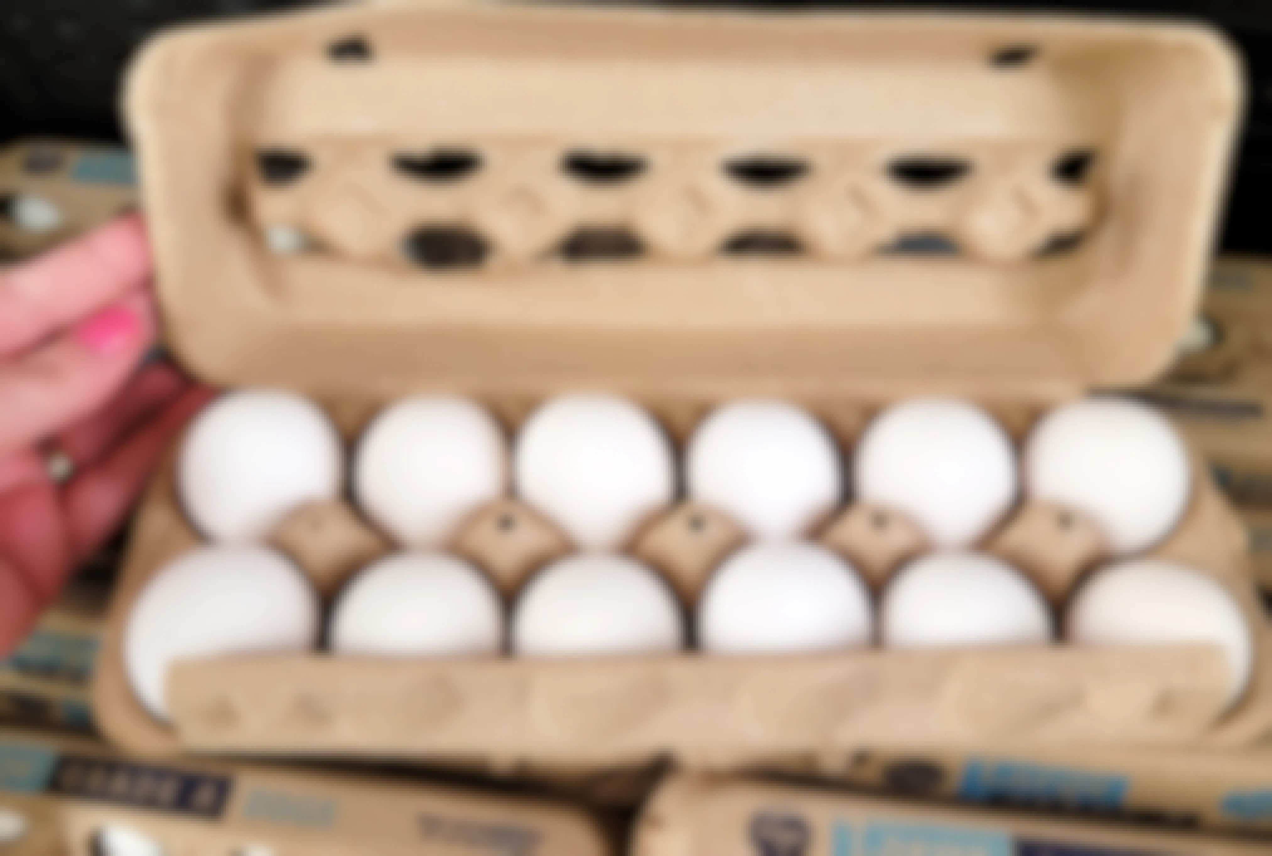 persons hand holding open a carton of a dozen eggs in a store