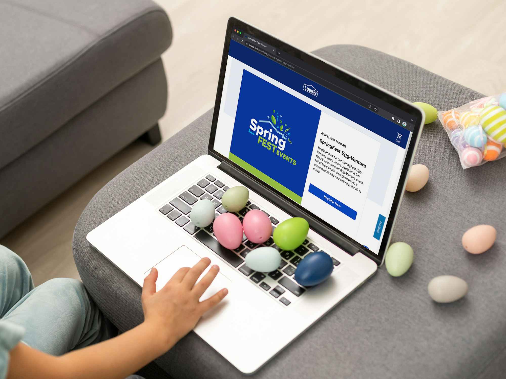 A laptop displaying the Lowe's SpringFest Egg-Venture event registration webpage with some colorful eggs on the keyboard and around the laptop