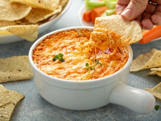 person dipping tortilla chip into bowl of buffalo chicken dip