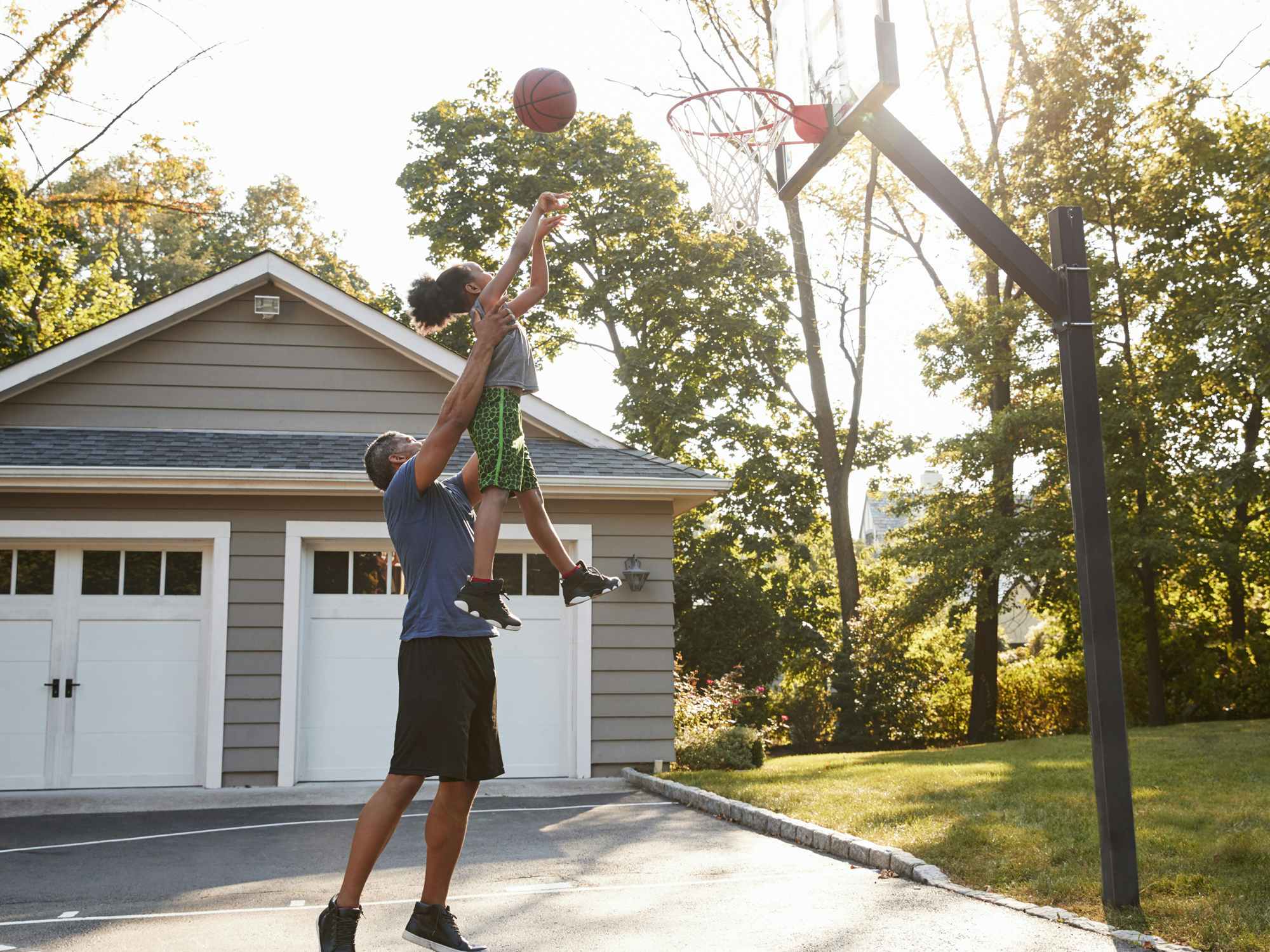 father playing basketball game with child in driveway