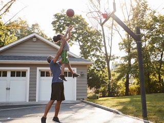 father playing basketball game with child in driveway