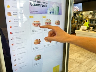 a person pointing at in store mcdonalds digital menu board