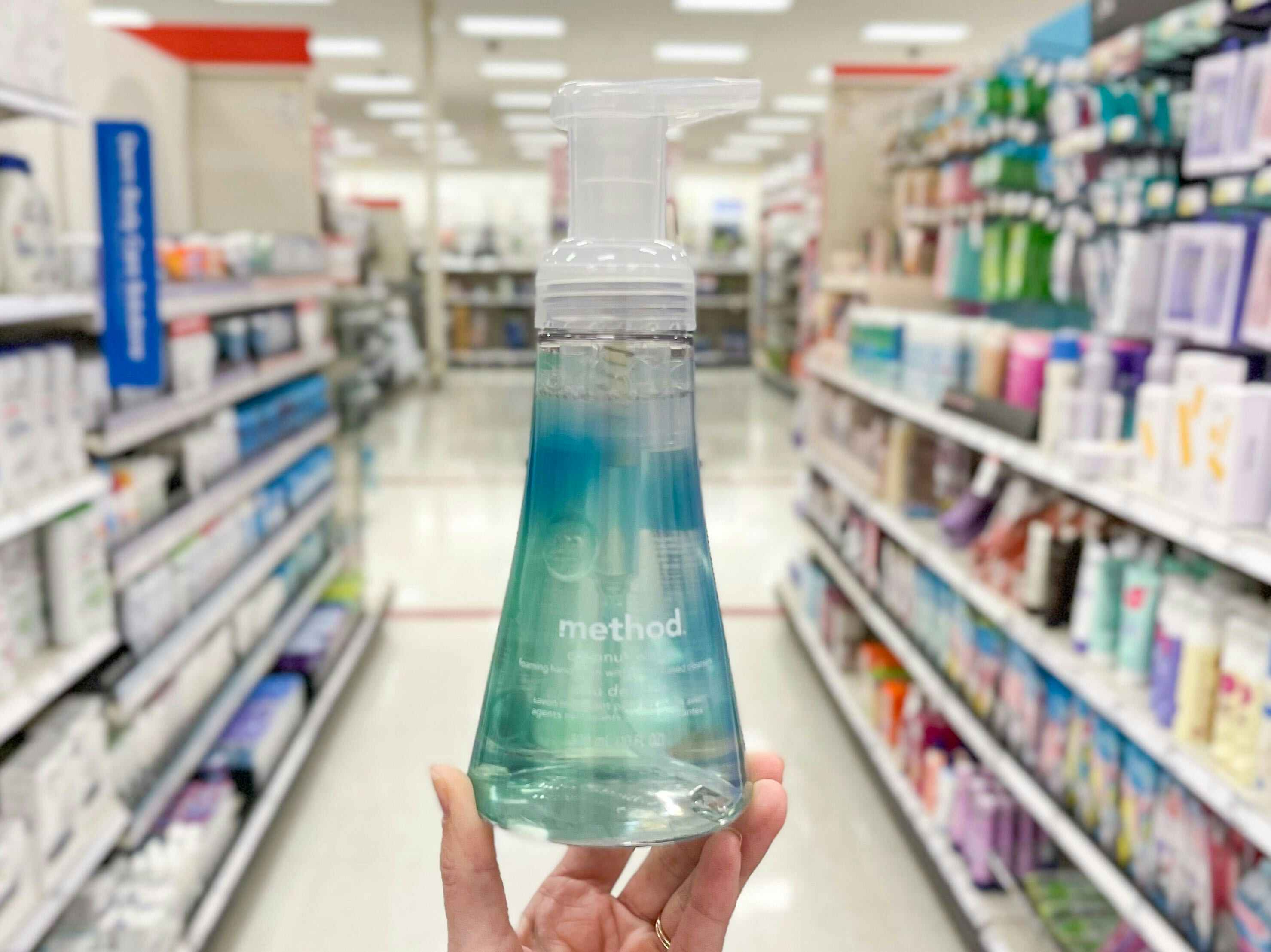 A Method hand soap held out by hand in front of a store aisle.