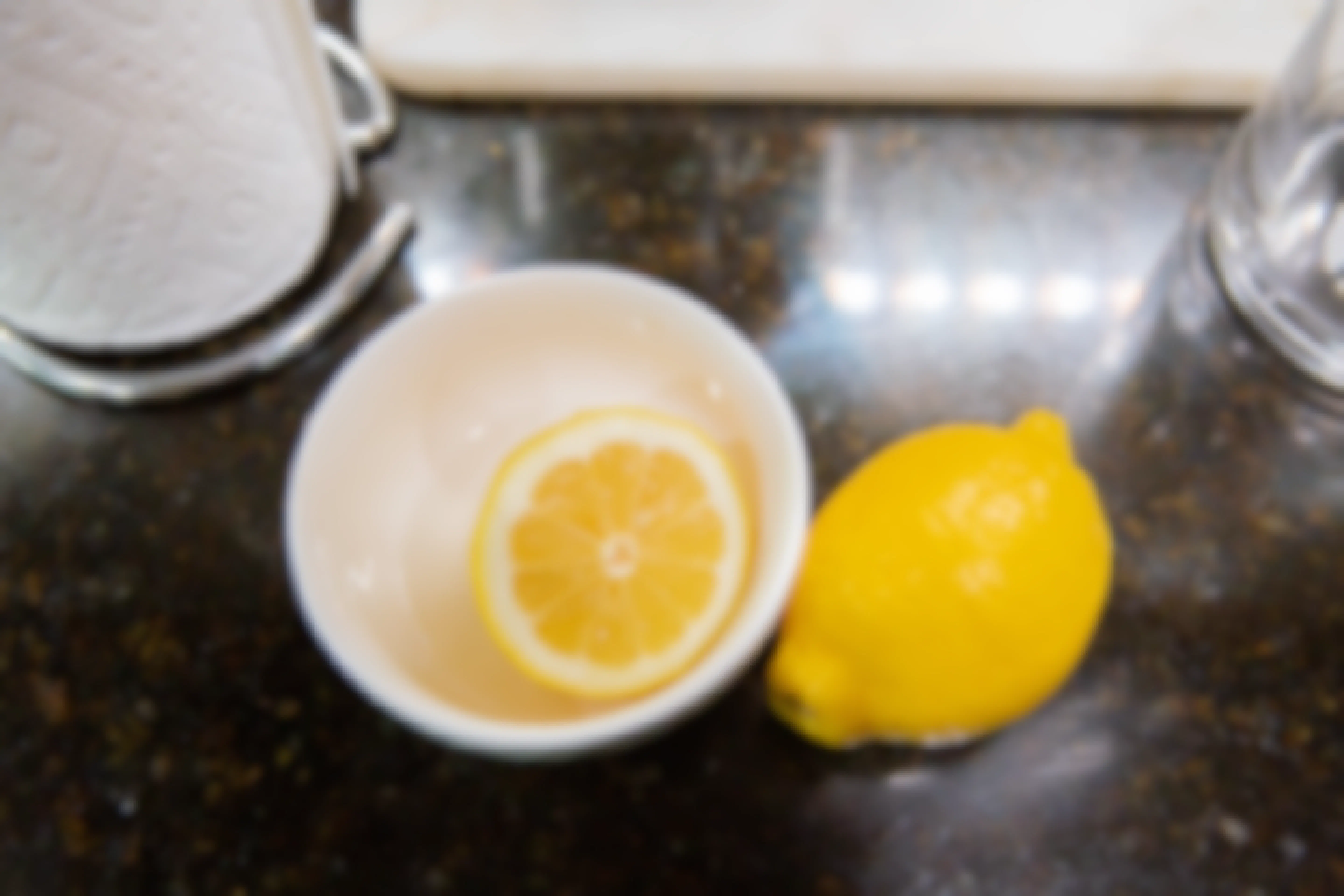 One half cut lemon in a bowl with a full lemon on a kitchen counter
