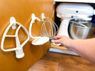 a person hanging up kitchenaid hooks on a cabinet door