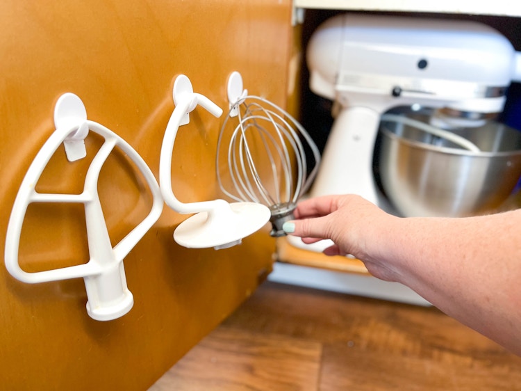 a person hanging up kitchenaid hooks on a cabinet door 