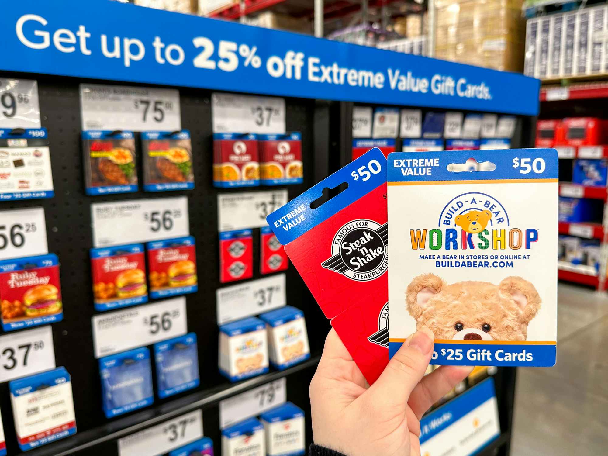 Someone holding up some gift cards in front of the Extreme Value gift card display in Sam's Club