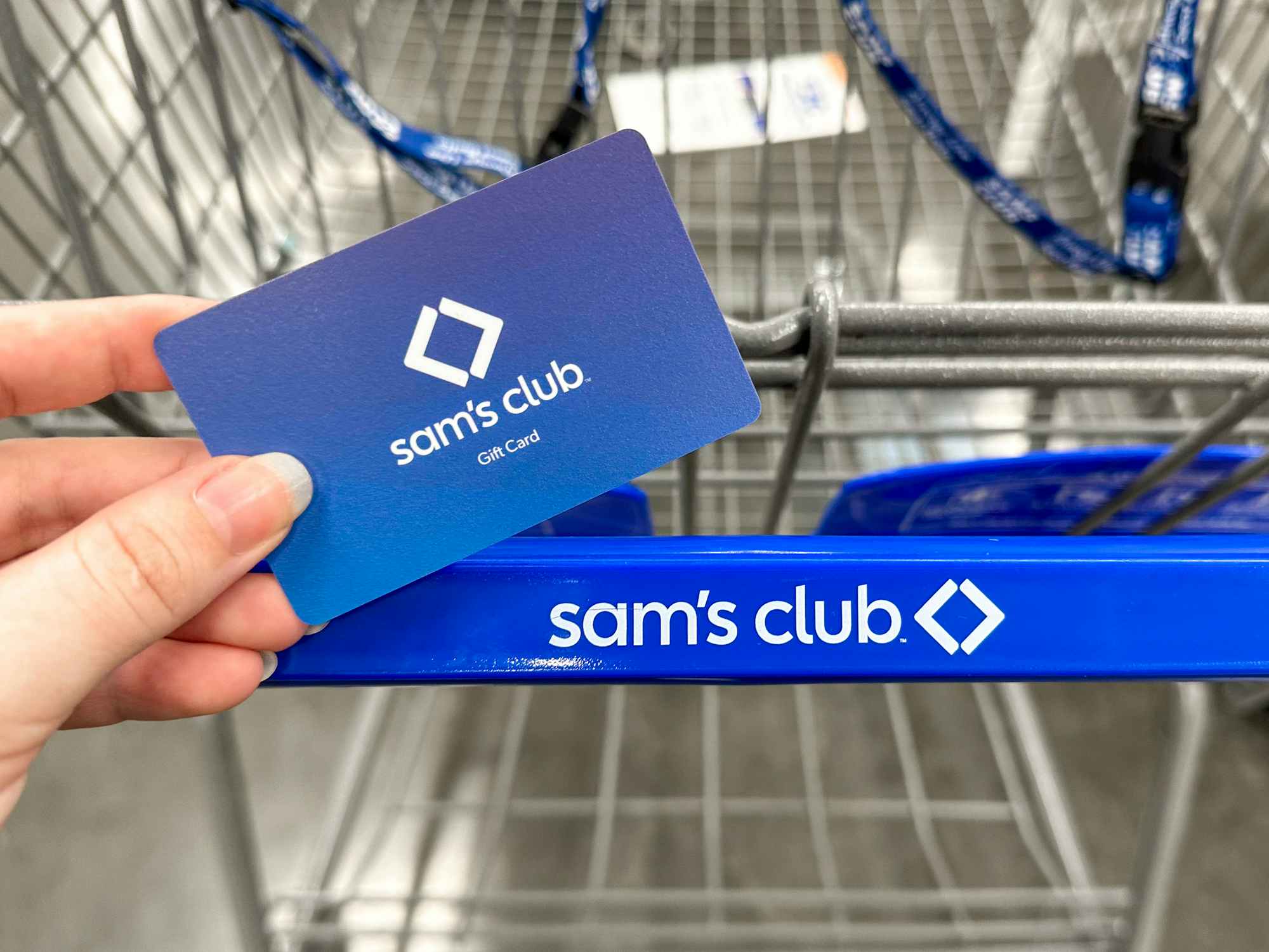 Someone holding a Sam's Club gift card near a cart