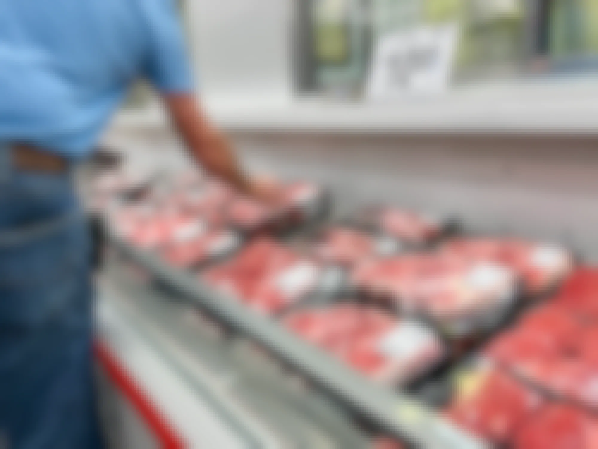 A Sam's Club employee stocking meat into a refrigerated display
