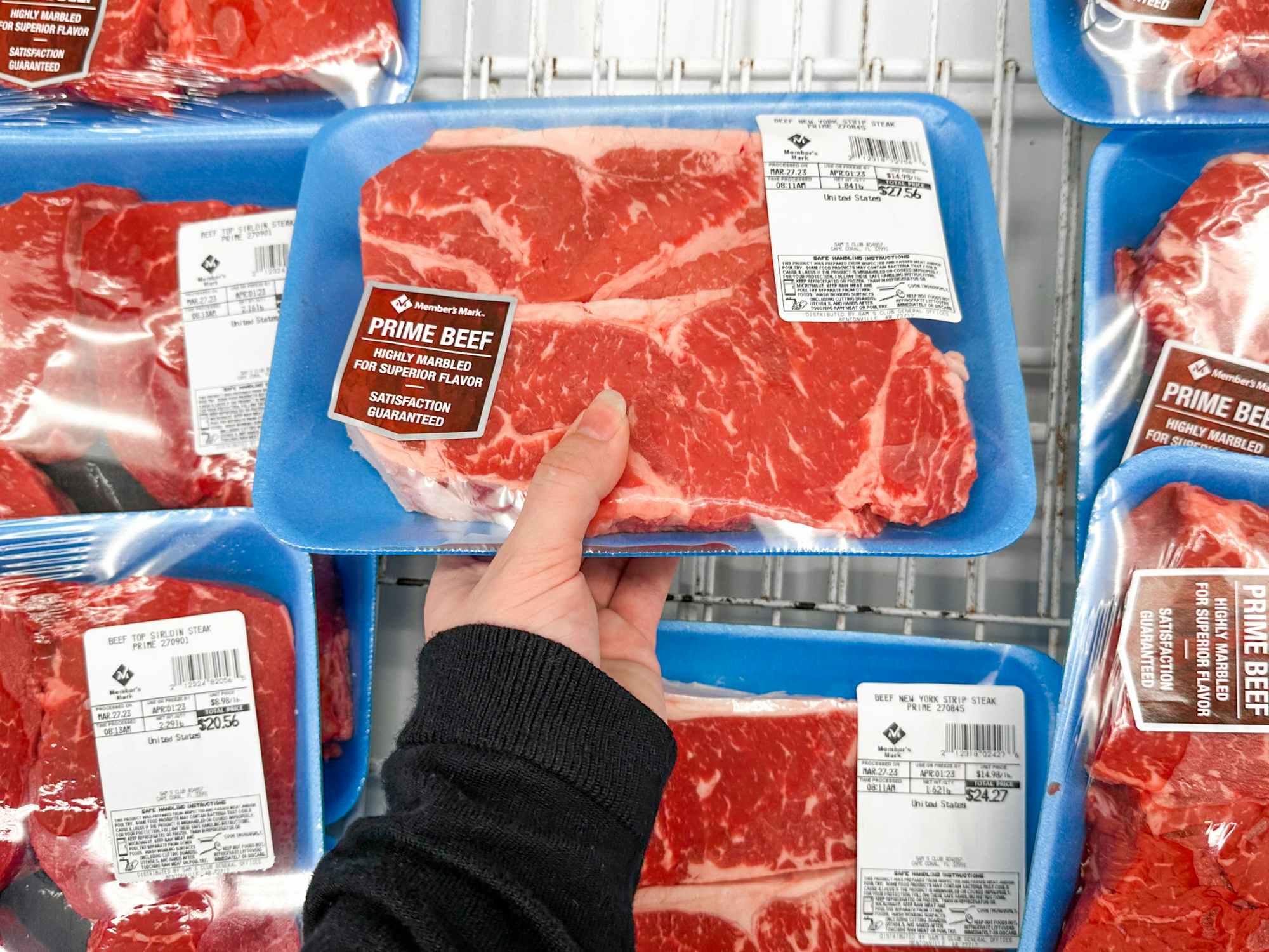 Someone picking out a package of USDA Prime beef from a refrigerator section in Sam's Club