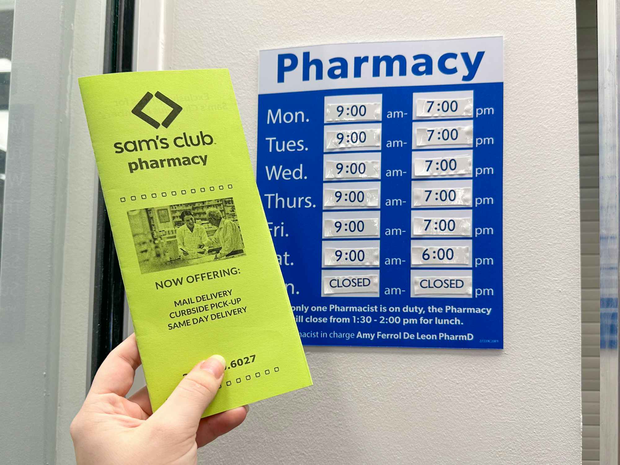 Someone holding a Sam's Club Pharmacy pamphlet in front of the Pharmacy hours