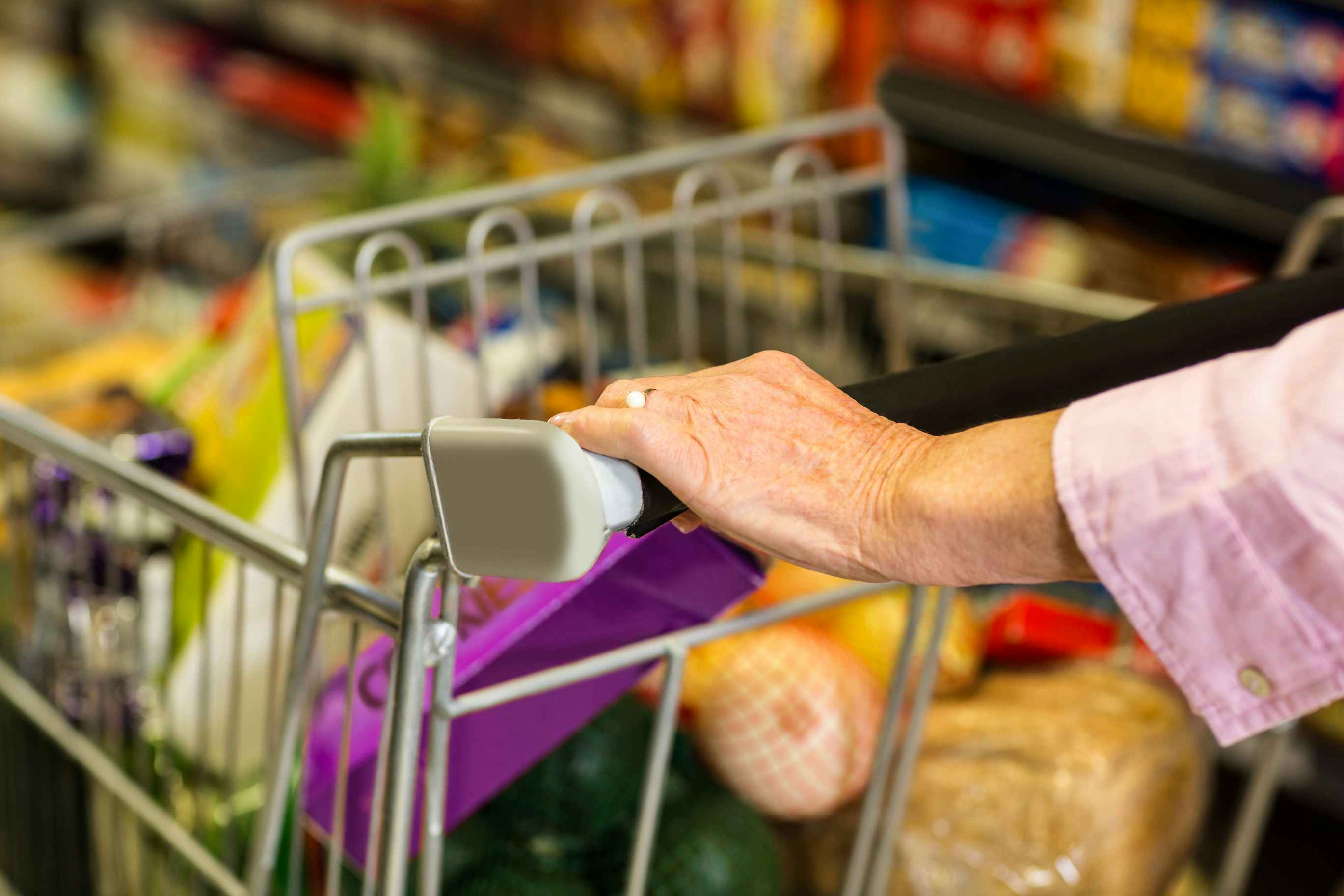 Close up of a senior woman's hand pushing a grocery cart.