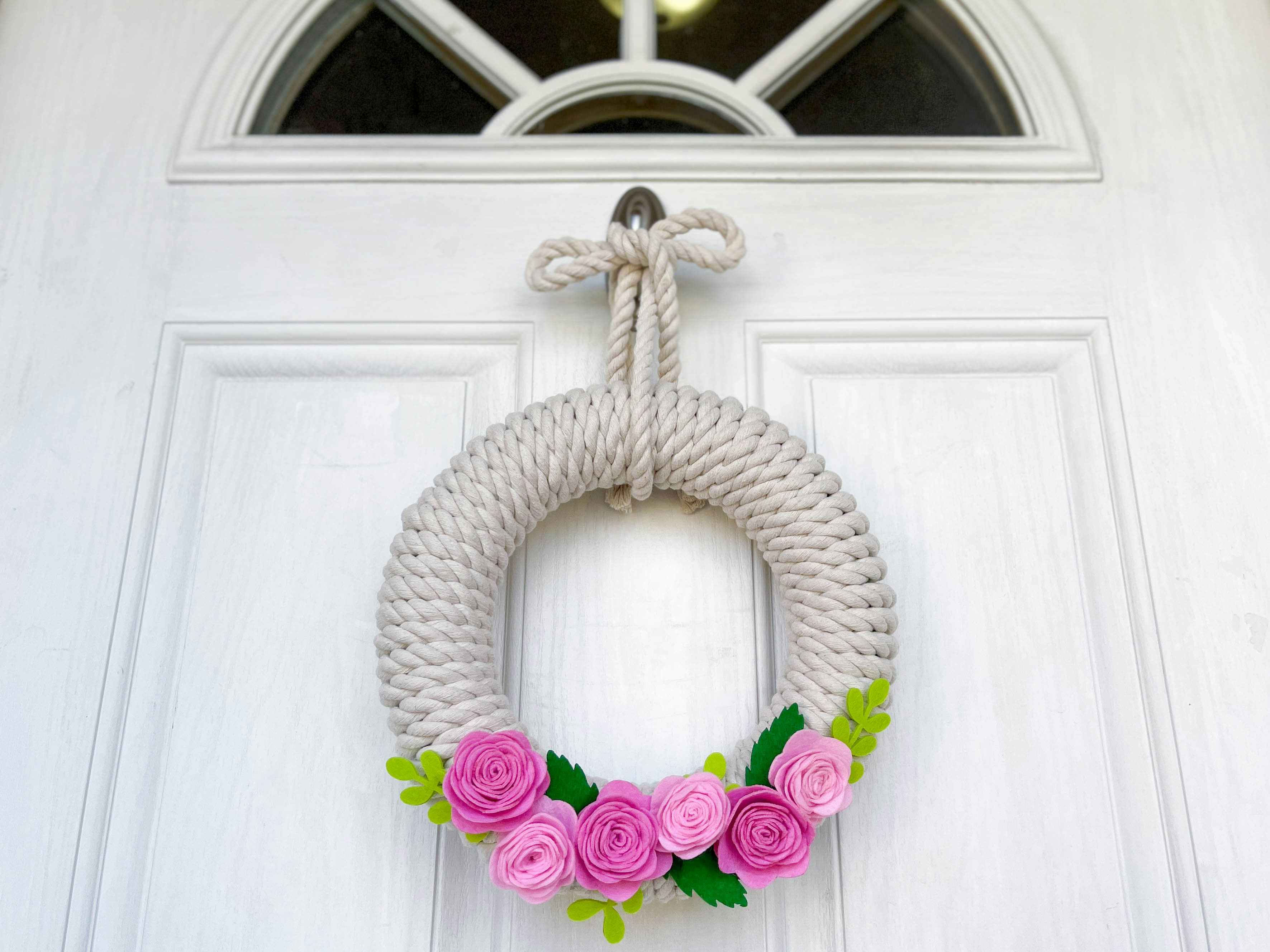 A rope and felt flower wreath hanging on a door 