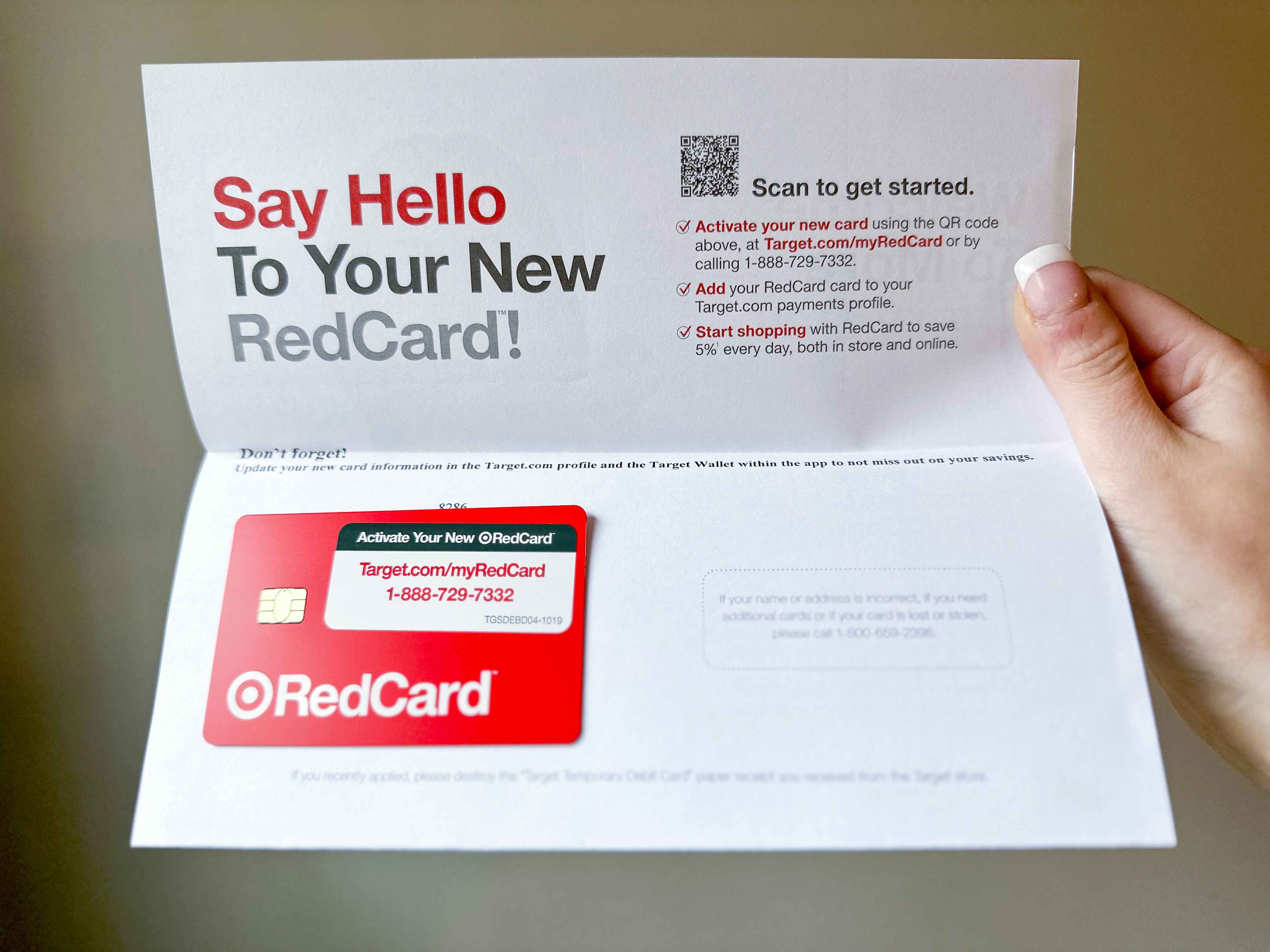 A woman's hang holding up the Target RedCard welcome letter that says "Say Hello To Your New RedCard" with the Target RedCard debit card attached to the letter