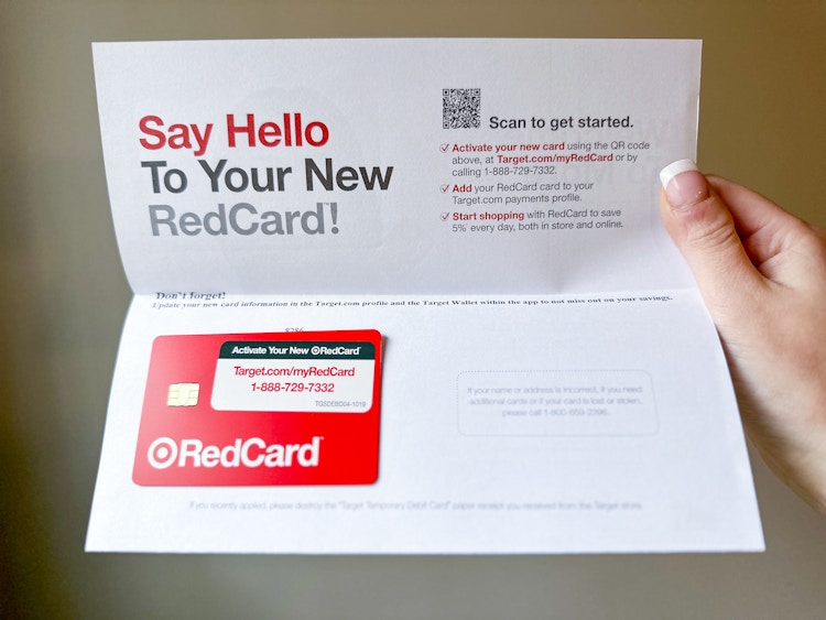 A woman's hang holding up the Target RedCard welcome letter that says "Say Hello To Your New RedCard" with the Target RedCard debit card attached to the letter