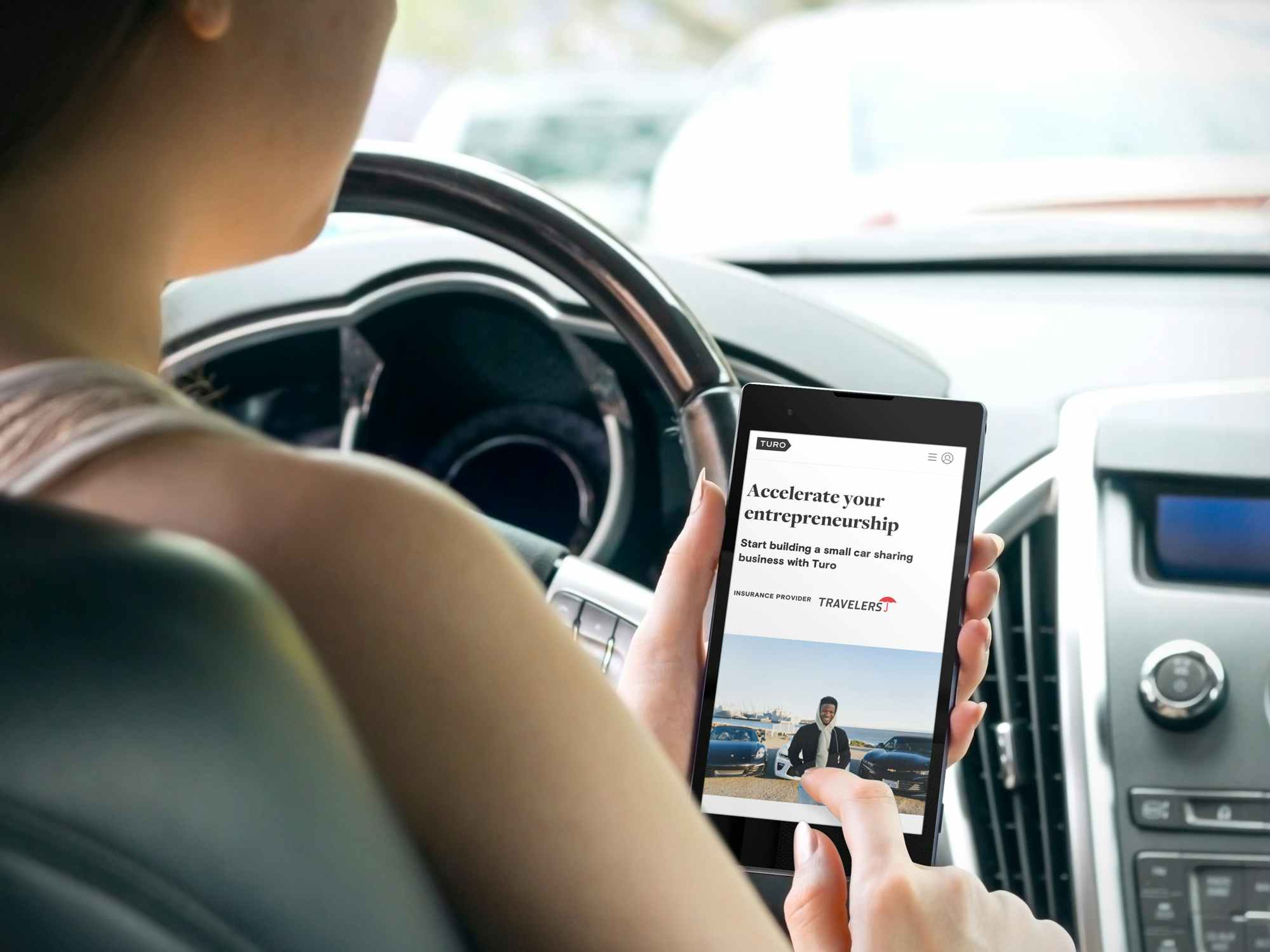 person in car looking at turo car sharing website on phone