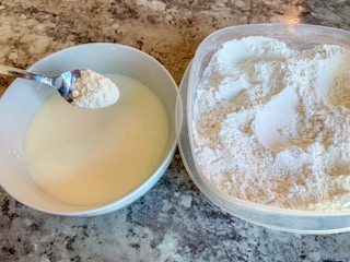 person adding powdered sugar into milk to make a glaze