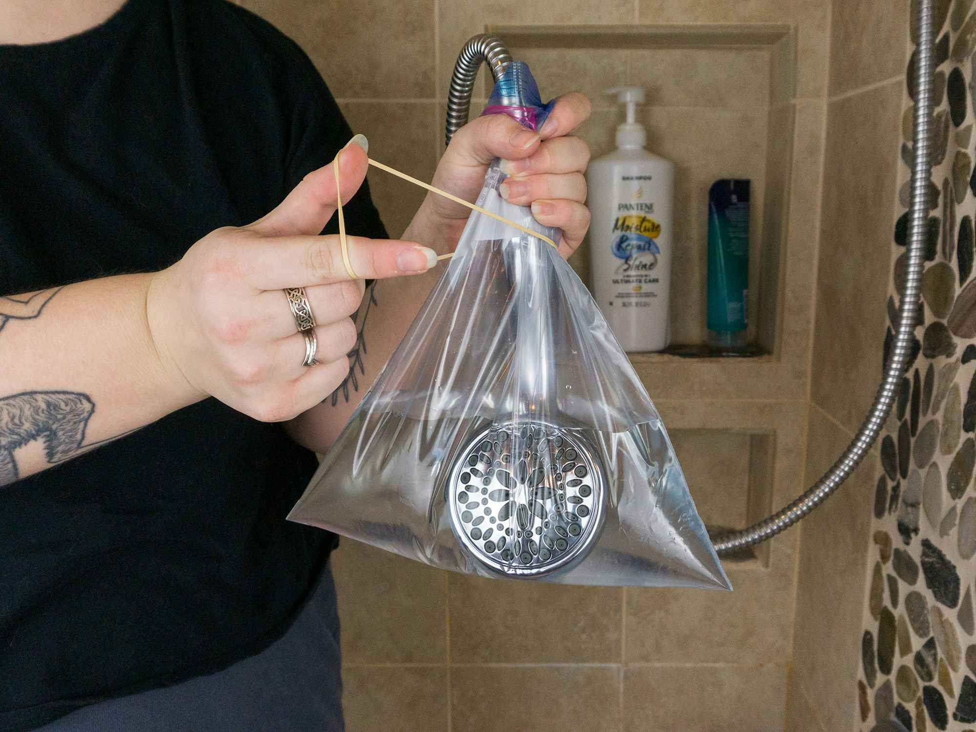 Someone putting a bag of vinegar onto their shower head and securing it with a rubber band
